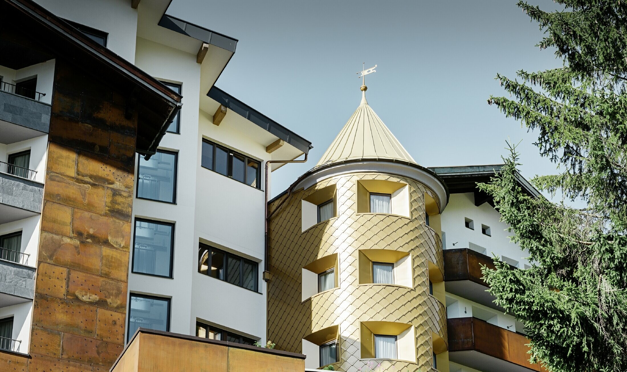 Tradičný hotel v Ischgl-e s drevenými balkónmi a drevenou fasádou a vežou so zlatými hliníkovými šablónami od firmy PREFA