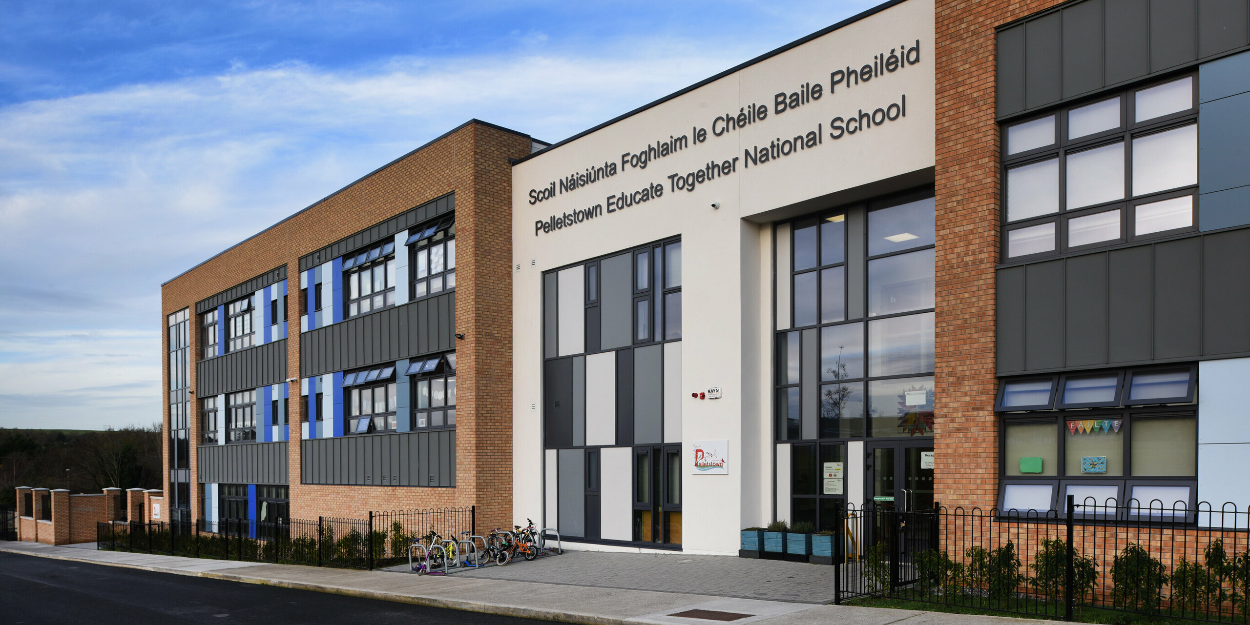 Detailansicht des Haupteingangs der Pelletstown Educate Together National School in Dublin. Die Aluminiumfassade aus PREFALZ P.10 hellgrau in Kombination mit Putz und Ziegeln sorgt für ein einzigartiges Erscheinungsbild und bietet der Schule eine langlebige und ästhetische Gebäudehülle.