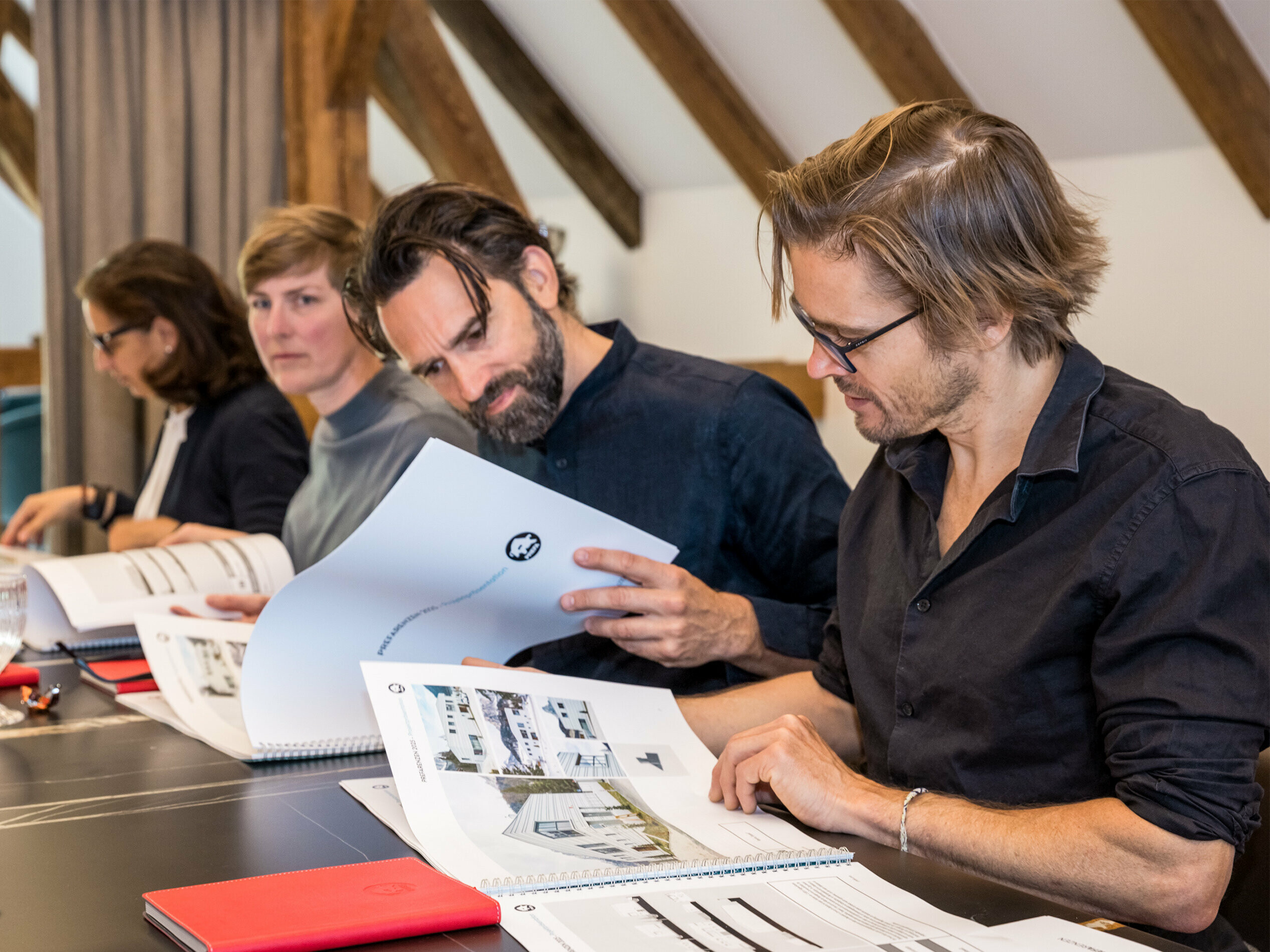 Porota zložená z architektov posudzuje dokumenty pre výber PREFARENZEN 2025. Členovia poroty sedia za stolom a prezerajú si podrobné prezentácie projektov.