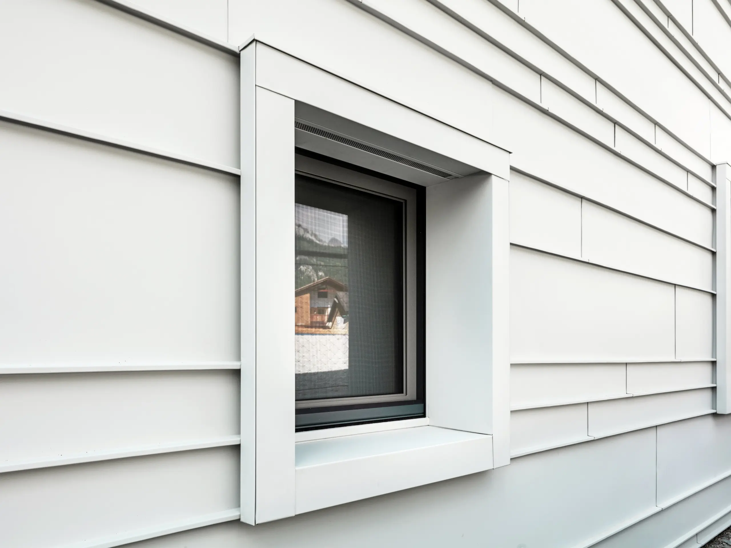 Detailný záber výrazných okenných výrezov v odvetranej fasáde z PREFALZ P.10 vo farbe prefa biela. Horizontálne položené hliníkové plechy dodávajú štruktúru, prehľadnosť a moderný vzhľad. Výrazné okenné rámy kasární „Tempesti” začínajú a končia vždy presne na línii ohybu. Tým sa zámerne zdôrazňuje štruktúra hliníka.