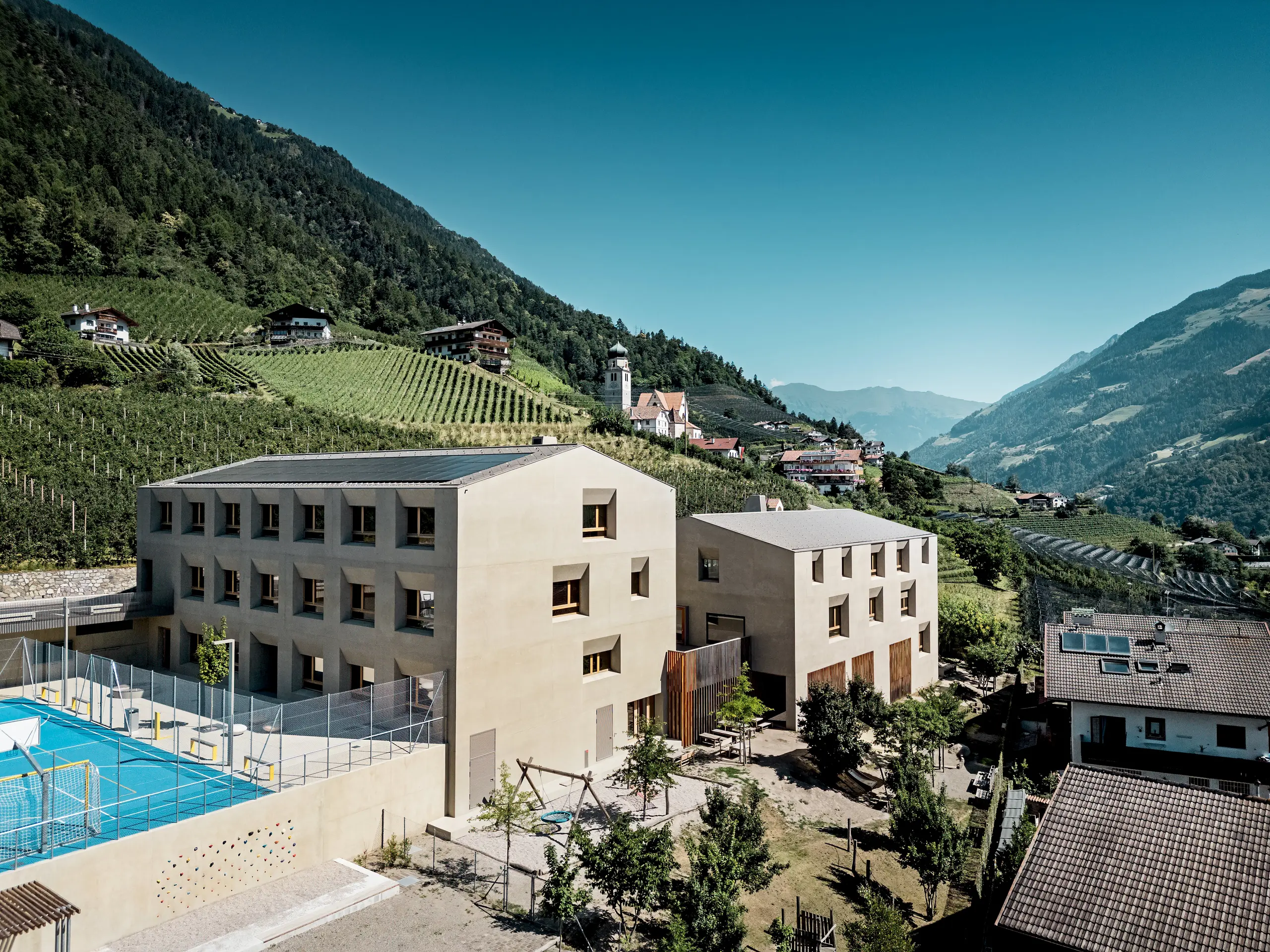 Vzdelávacie centrum Riffian v Južnom Tirolsku tvorí materská a základná škola, ktoré spolu vytvárajú harmonický architektonický celok zasadený do horskej krajiny. Strešné šablóny PREFA 44 × 44 v odtieni P.10 bronzová dodávajú budovám elegantný vzhľad, poskytujú dlhodobú ochranu pred poveternostnými vplyvmi a prirodzene zapadajú do okolitého prostredia.