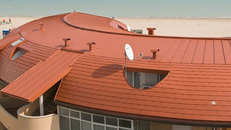 Zaoblená strecha obytného komplexu pokrytá šindľom PREFA a strechou so stojatou drážkou (falcom) – Prefalz – od spoločnosti PREFA v tehlovočervenej farbe.