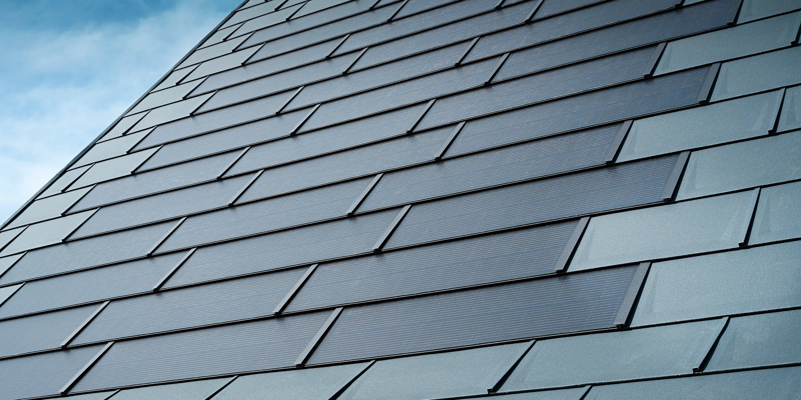 Detailný pohľad na zrekonštruovanú strechu rodinného domu v Leondingu s integrovanými solárnymi panelmi PREFA v antracitovej farbe. Detailný záber ukazuje vysokokvalitné plechové panely od spoločnosti PREFA, ktoré umožňujú bezproblémovú integráciu solárnych modulov. Toto trvanlivé riešenie odolné voči poveternostným vplyvom ponúka udržateľný a energeticky efektívny spôsob výroby elektrickej energie. Obrázok ilustruje estetickú a funkčnú kvalitu použitých hliníkových plechov. Okolo inovatívnych solárnych strešných panelov boli položené klasické strešné panely R.16 v rovnakej farbe.
