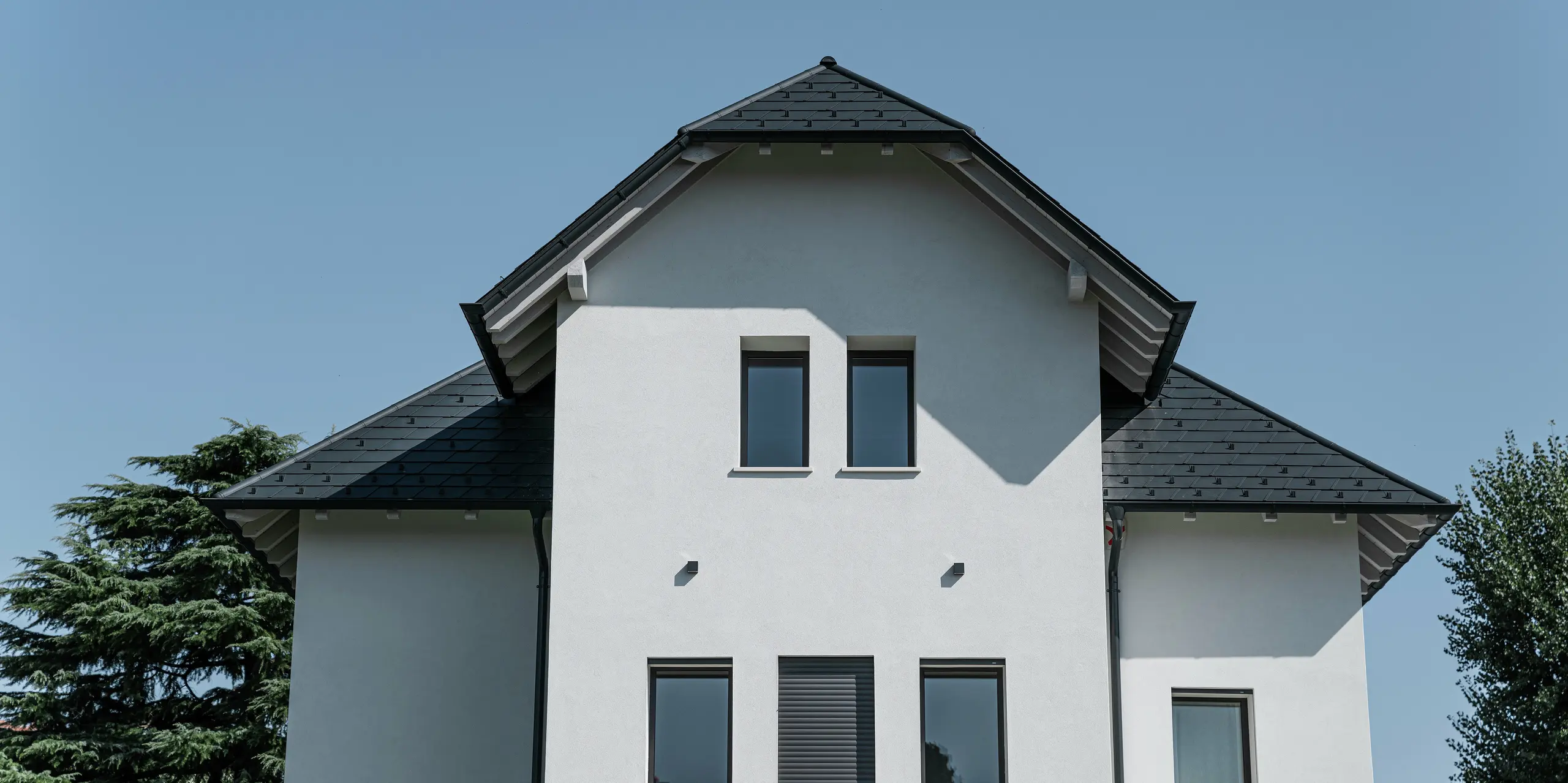 Detailný pohľad na predný štít moderného rodinného domu v Marano Vicentino v Taliansku s PREFA strechou zo strešných šindľov v antracitovej farbe P.10. Výrazný tvar strechy a vysoko kvalitné hliníkové produkty zaisťujú elegantné a trvácne riešenie strechy na trojposchodovej budove.