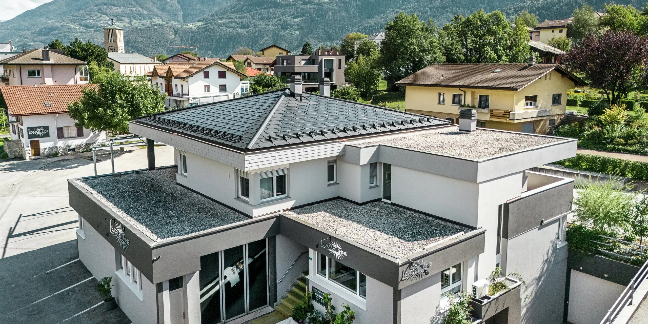 Elegantná hliníková strecha PREFA dodáva vinárstvu Leukersonne v Sustene (CH) moderný vzhľad a poskytuje optimálnu ochranu pred poveternostnými vplyvmi. Integrované solárne panely PREFA zabezpečujú udržateľnú výrobu energie bez toho, aby narušili vzhľad strechy. Strešnú plochu dotvárajú strešné panely PREFA R.16. Prvé poschodie a zvyšná časť prvého poschodia sú pokryté pochôdznym štrkovým povrchom.