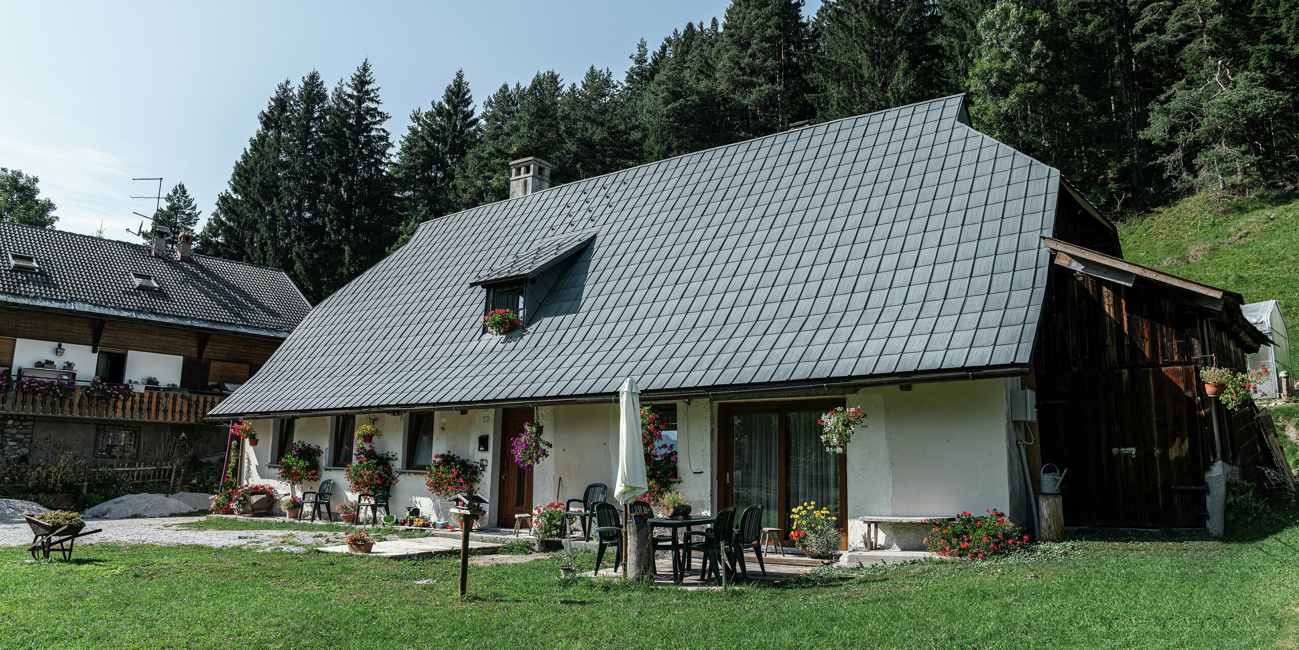 Očarujúci rodinný dom v Tarvisu v Taliansku, od roku 1972 pokrytý odolnými falcovanými škridlami PREFA: Veľká valbová strecha s odolnou hliníkovou krytinou spoľahlivo chráni dom už desaťročia pred alpskými poveternostnými vplyvmi. Kvitnúce kvetináče zdobia rustikálnu fasádu, útulná terasa so záhradným nábytkom láka k oddychu. V pozadí husté zelené ihličnaté stromy vytvárajú idylickú atmosféru a dokonale začleňujú dom do prírodného prostredia.