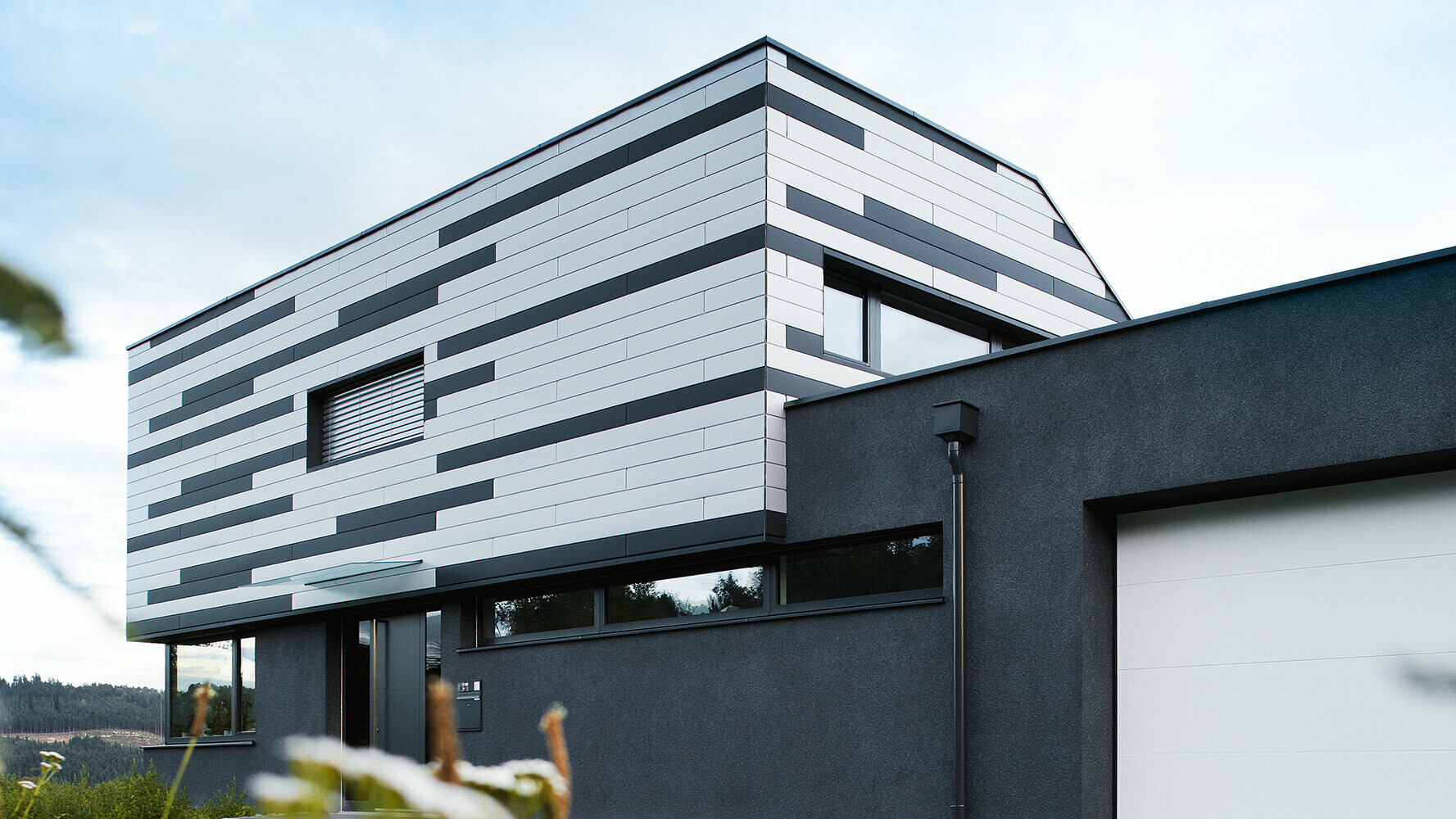 Moderný rodinný dom s kreatívnym dizajnom fasády; fasádne prvky PREFA Sidings boli položené striedaním farieb strieborná a antracitová matná.