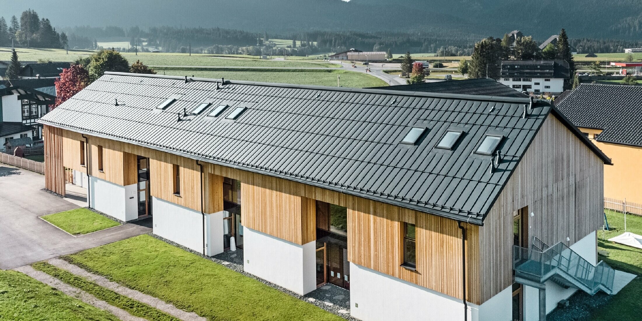 Materská škola Kräuterkindergarten in Bad Mitterndorf s veľkou strechou PREFALZ vo farebnom vyhotovení P.10 antracitová a drevenou fasádou