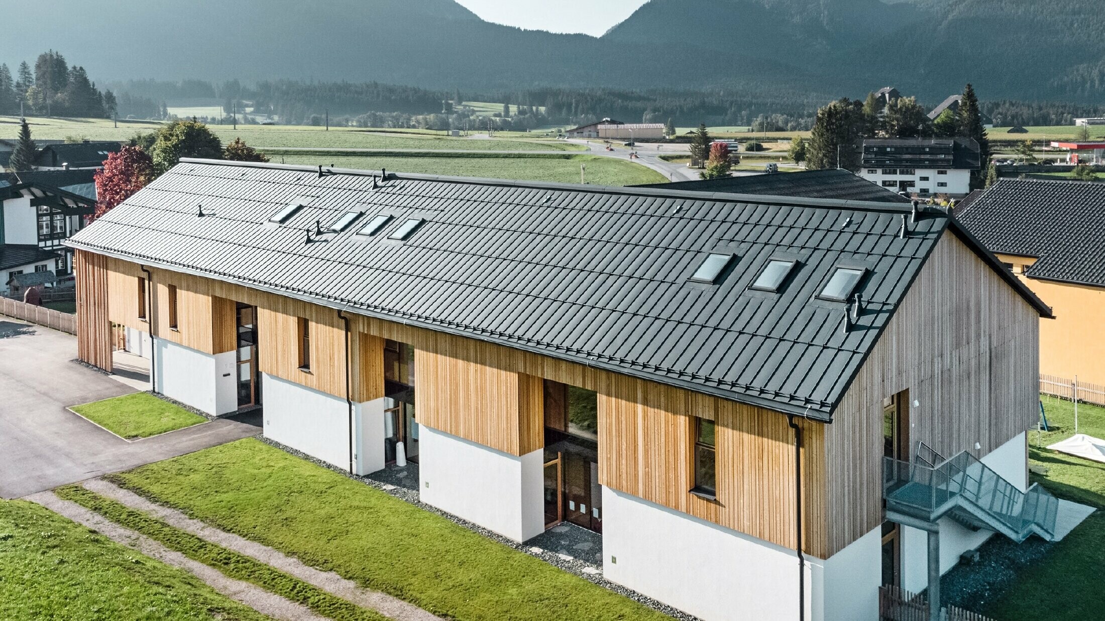 Materská škola Kräuterkindergarten in Bad Mitterndorf s veľkou strechou PREFALZ vo farebnom vyhotovení P.10 antracitová a drevenou fasádou