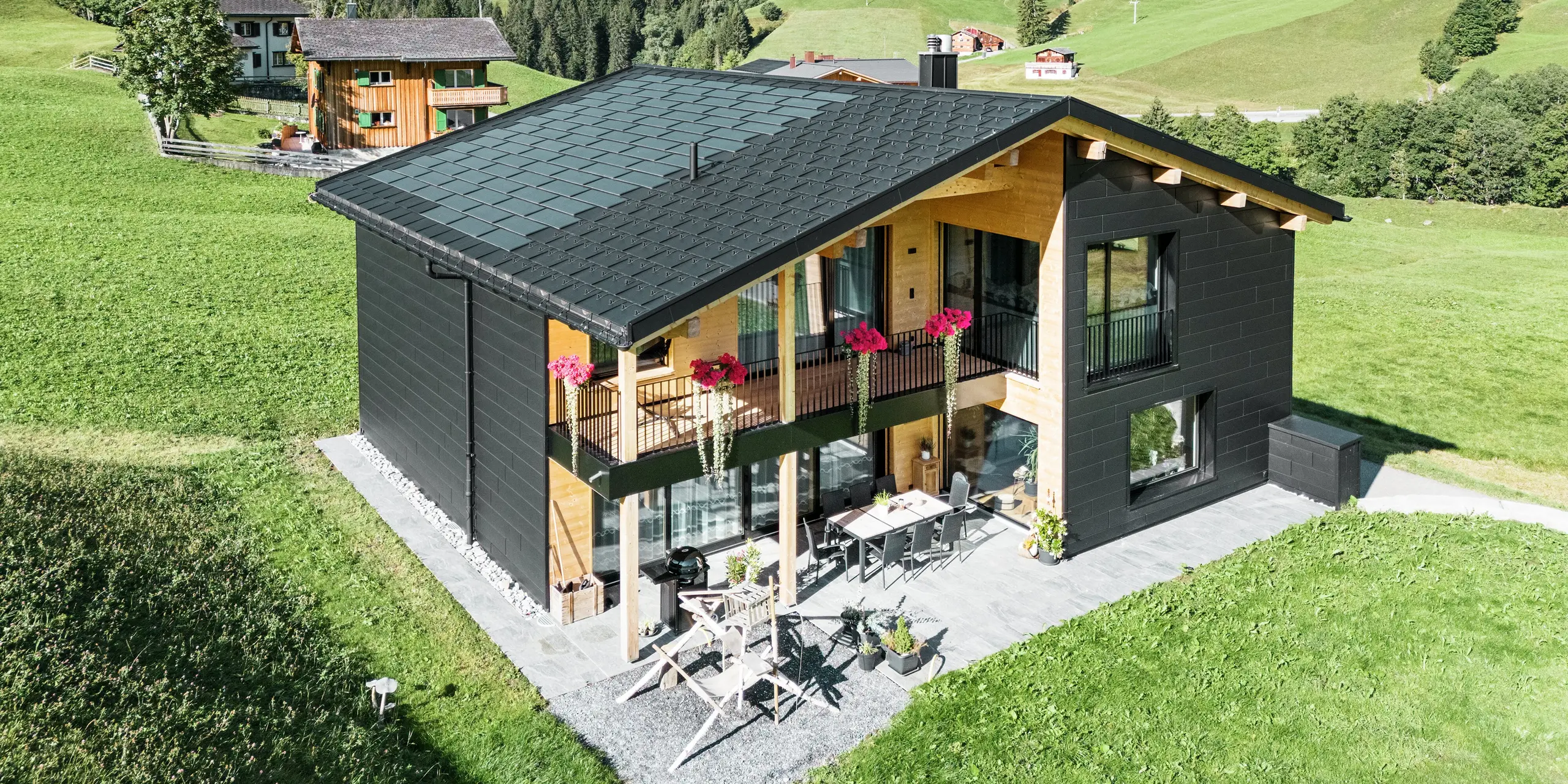 Elegantný rodinný dom v kopcovitej oblasti Ascharina (Švajčiarsko) ukazuje, ako sa dá perfektne skombinovať hliník a drevo. Robustné fasádne panely PREFA Siding.X v čiernej farbe P.10 harmonizujú so strechou z integrovaných solárnych panelov PREFA a strešných panelov R.16 v rovnakom farebnom odtieni. Odolný hliníkový plášť spoľahlivo chráni budovu pred nástrahami alpského podnebia.