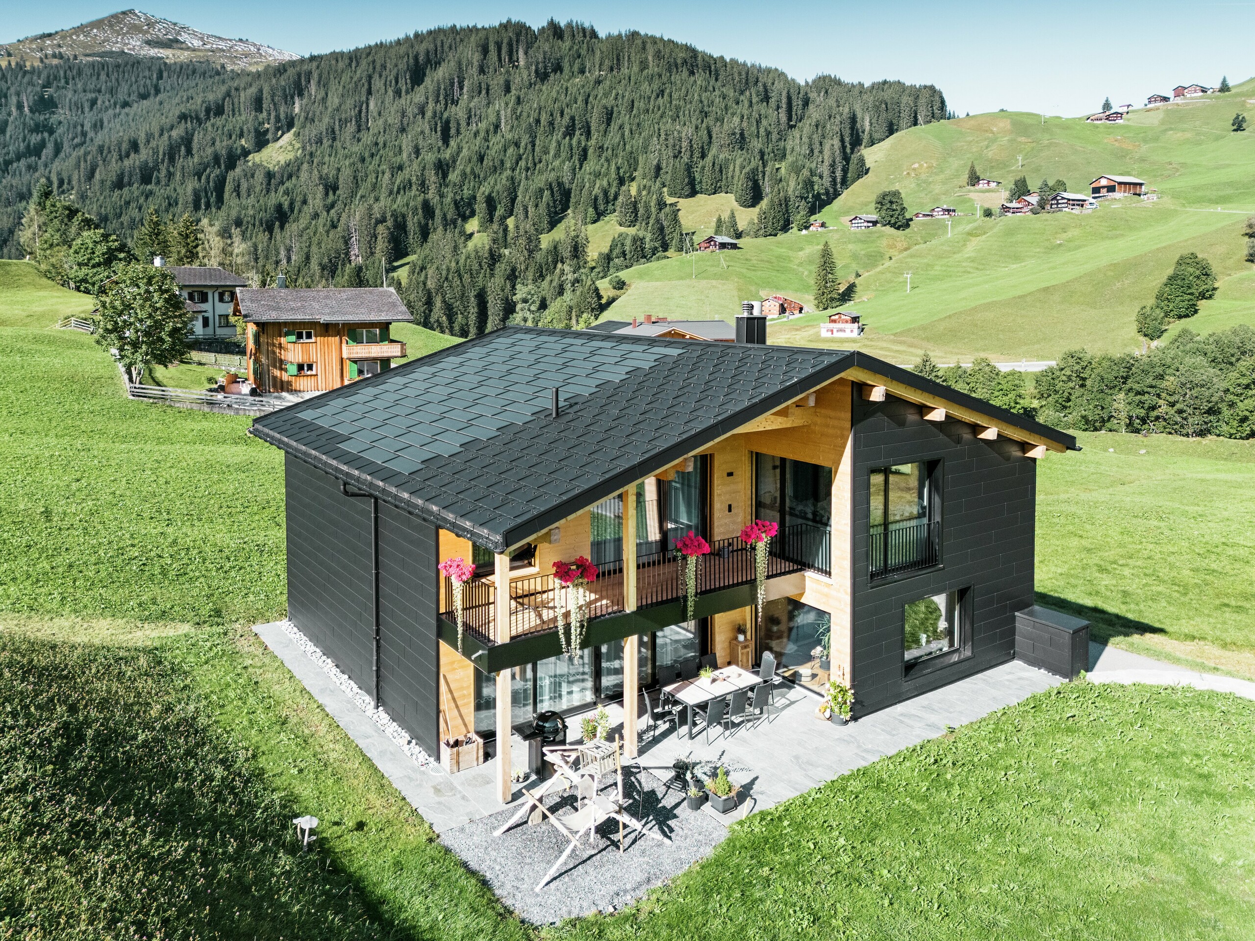 Elegantný rodinný dom v kopcovitom prostredí Ascharina (Švajčiarsko) ukazuje, ako sa dá dokonale skombinovať hliník a drevo. Robustné fasádne panely PREFA Siding.X v čiernej farbe P.10 harmonizujú so strechou z integrovaných solárnych panelov PREFA a strešných panelov R.16 v rovnakej farebnej povrchovej úprave. Odolný hliníkový obklad spoľahlivo chráni budovu pred nástrahami alpského podnebia.