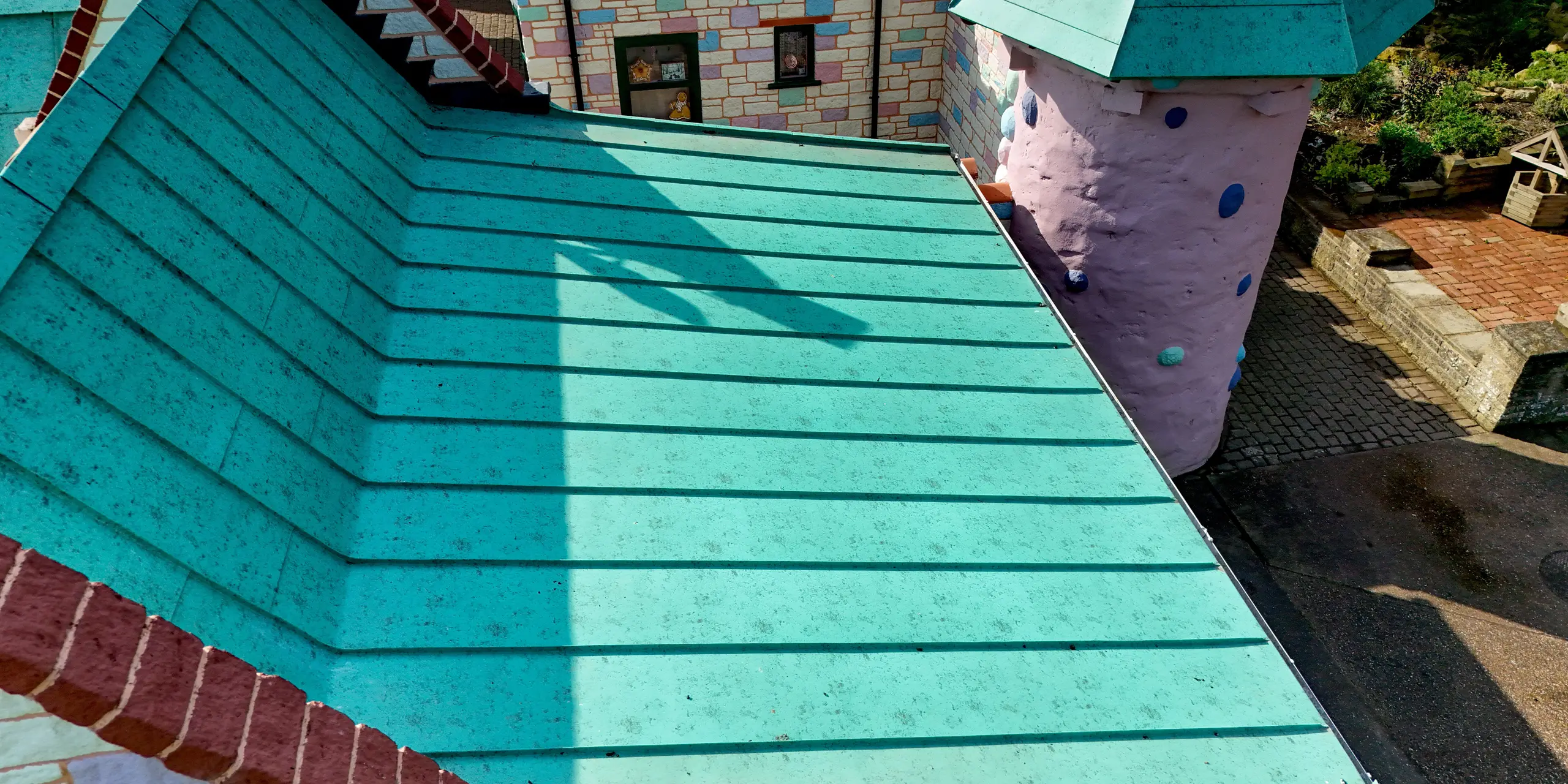 Detailaufnahme eines PREFALZ Stehfalzdachs im Sundown Adventureland mit klaren, parallel verlaufenden Falzlinien als prägnante visuelle Struktur. Die Aluminiumoberfläche in P.10 Patinagrün wirkt als starker Eyecatcher und unterstreicht die moderne Präzision trotz verspielter Schlossarchitektur. Sauber ausgeführte Kanten und Übergänge zeigen die hohe Verarbeitungsqualität. Das PREFA Dach überzeugt dabei nicht nur optisch, sondern auch funktional durch hohe Langlebigkeit, Korrosionsbeständigkeit und zuverlässigen Schutz gegenüber Wind und Wetter.