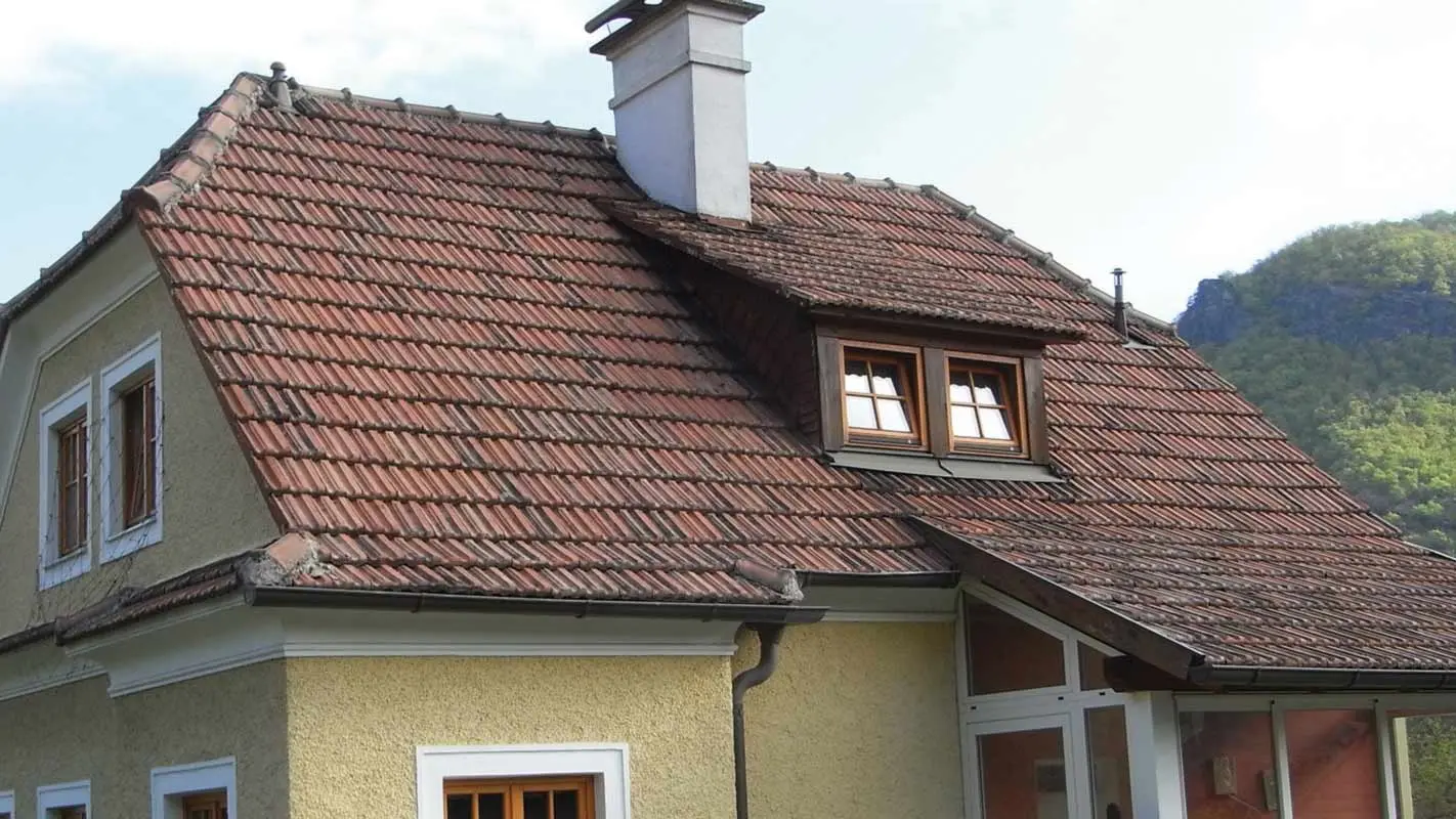 Starý rodinný dom s hrubou žltou omietkovou fasádou pred rekonštrukciou strechy z pálených škridiel