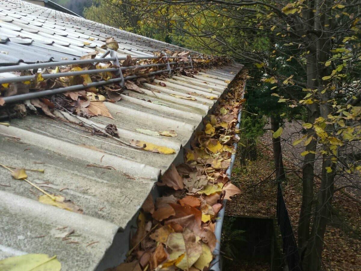 Strešný žľab s množstvom jesenného lístia, čistenie upchatých žľabov