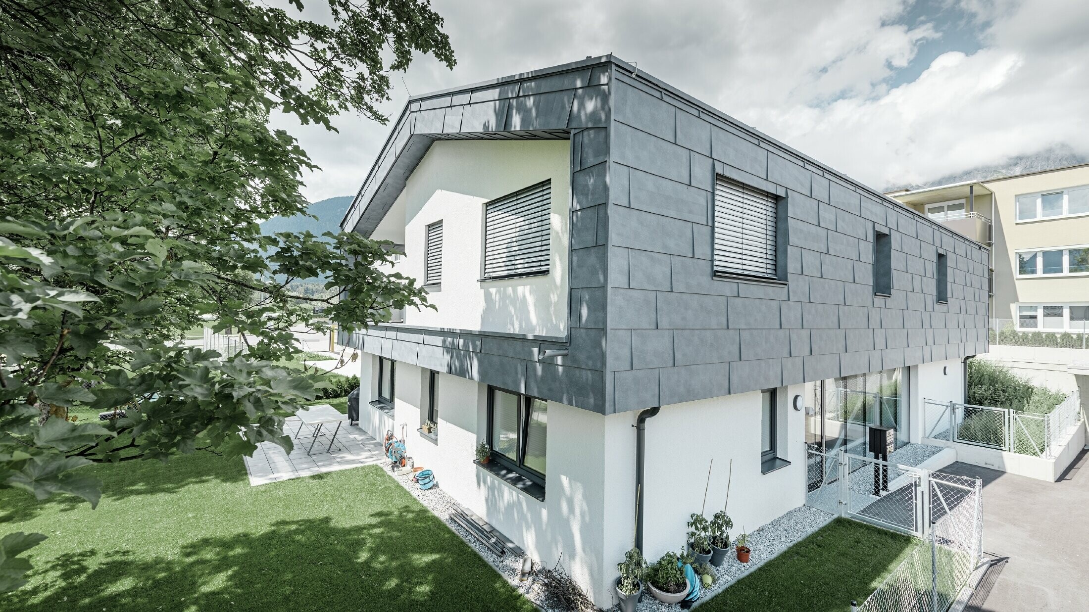 Moderná nadstavba obytného domu s plochou sedlovou strechou bez okapu; fasádny obklad bol realizovaný pomocou fasádnych panelov PREFA FX.12 v kamenné šedej.