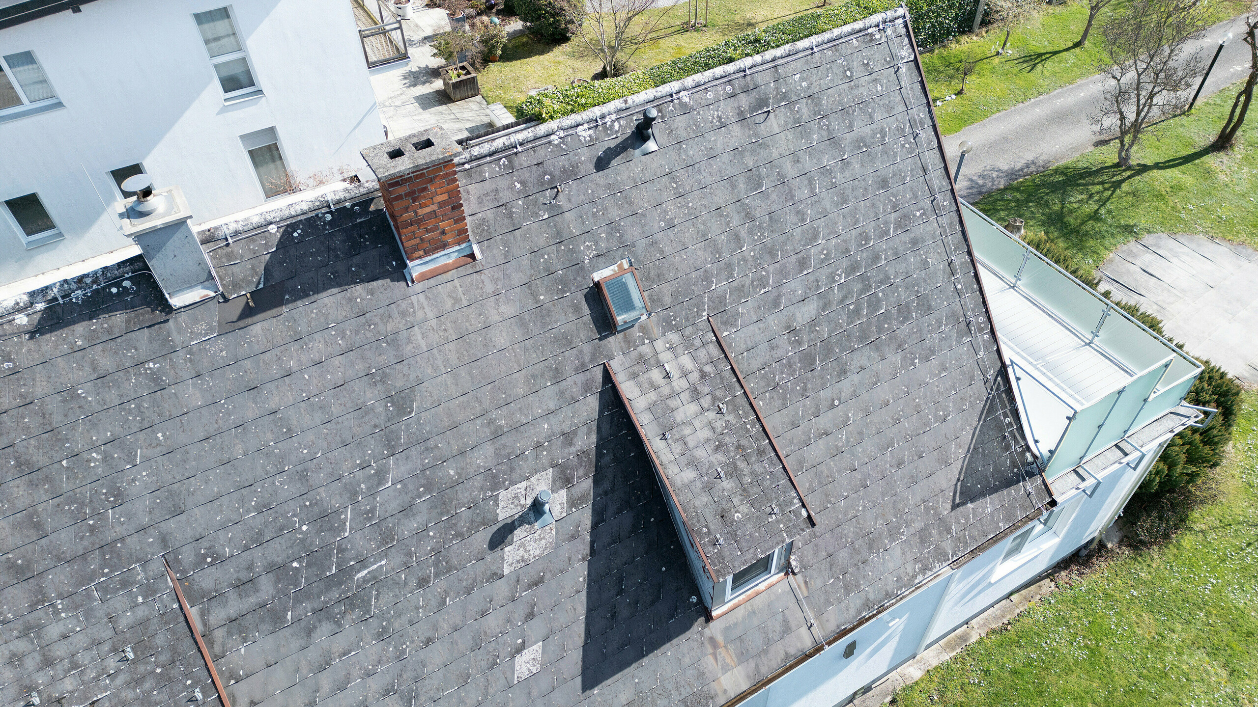 Strecha rodinného domu v Leondingu pred renováciou s integrovanými solárnymi panelmi PREFA v antracitovej farbe. Na obrázku je stará opotrebovaná strecha Eternit z vtáčej perspektívy z bočného pohľadu. Viditeľné poškodenia a opotrebovanie zdôrazňujú potrebu renovácie strechy a inštalácie moderného, udržateľného solárneho systému. Tento obrázok znázorňuje počiatočný stav pred premenou na energeticky účinnú strešnú konštrukciu odolnú voči poveternostným vplyvom.