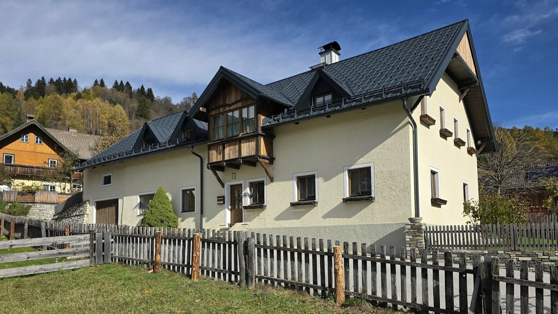 Unter einem strahlend blauen Himmel erstrahlt ein frisch saniertes Landhaus mit einem modernen PREFA Aluminiumdach. Die bewährten PREFA Dachplatten verleihen dem Gebäude ein hochwertiges und langlebiges Erscheinungsbild. Besonders ins Auge fallen die elegante Dachentwässerung, die gleichmäßig verlegten Schneestopper und die perfekt integrierten Gauben. Die robuste PREFA-Oberfläche schützt das Gebäude dauerhaft vor Witterungseinflüssen und sorgt für einen dauerhaft gepflegten Eindruck. Die klare Architektur und die natürliche Umgebung ergeben eine harmonische Szenerie, in der Funktionalität und Ästhetik perfekt zusammenspielen.