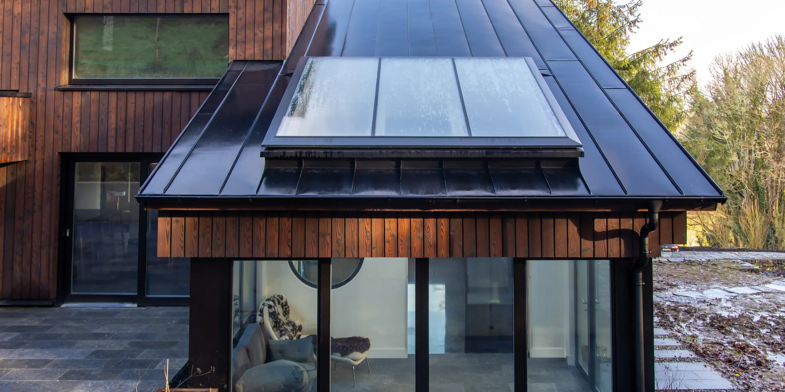 Detailaufnahme des Wintergartens am House of Holywell in Sligo: Aus der frontalen Perspektive richtet sich der Blick auf das präzise ausgeführte PREFALZ Aluminiumdach in P.10 Schwarz, das sich elegant über die kompakte Dachform spannt. Die klaren Stehfalze strukturieren die Fläche und rahmen das großzügige Dachfenster ein. Die glatte Oberfläche reflektiert das Licht und betont die hochwertige Verarbeitung. PREFA Aluminium überzeugt durch Langlebigkeit, Korrosionsbeständigkeit und zuverlässigen Schutz bei wechselhaften Witterungsbedingungen.