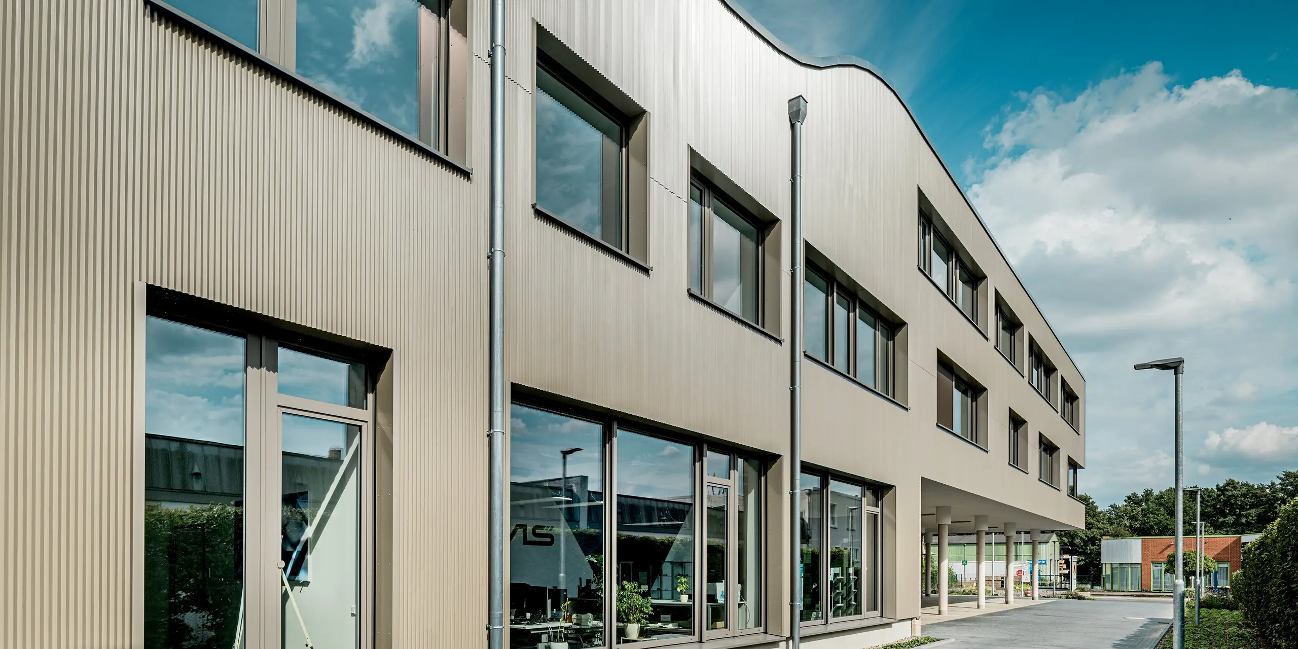 Das Bild zeigt das moderne Festo-Gebäude in Langenhagen, dessen prägnante Fassade mit PREFA Strangpressprofilen in Zackenform beeindruckt. Die Zacken verleihen der Fassade eine markante Textur und sorgen für eine einzigartige optische Wirkung. Die wellenartige Struktur des Gebäudes hebt sich eindrucksvoll vom klaren, geometrischen Design ab und fügt sich harmonisch in die Umgebung ein. Die große Glasfläche und die eleganten Aluminium Verbundplatten ergänzen das Fassadendesign perfekt und bieten eine moderne, zeitlose Ästhetik. Dank der langlebigen und pflegeleichten PREFA Materialien ist die Fassade optimal vor Witterungseinflüssen geschützt und bleibt über Jahre hinweg in einwandfreiem Zustand.