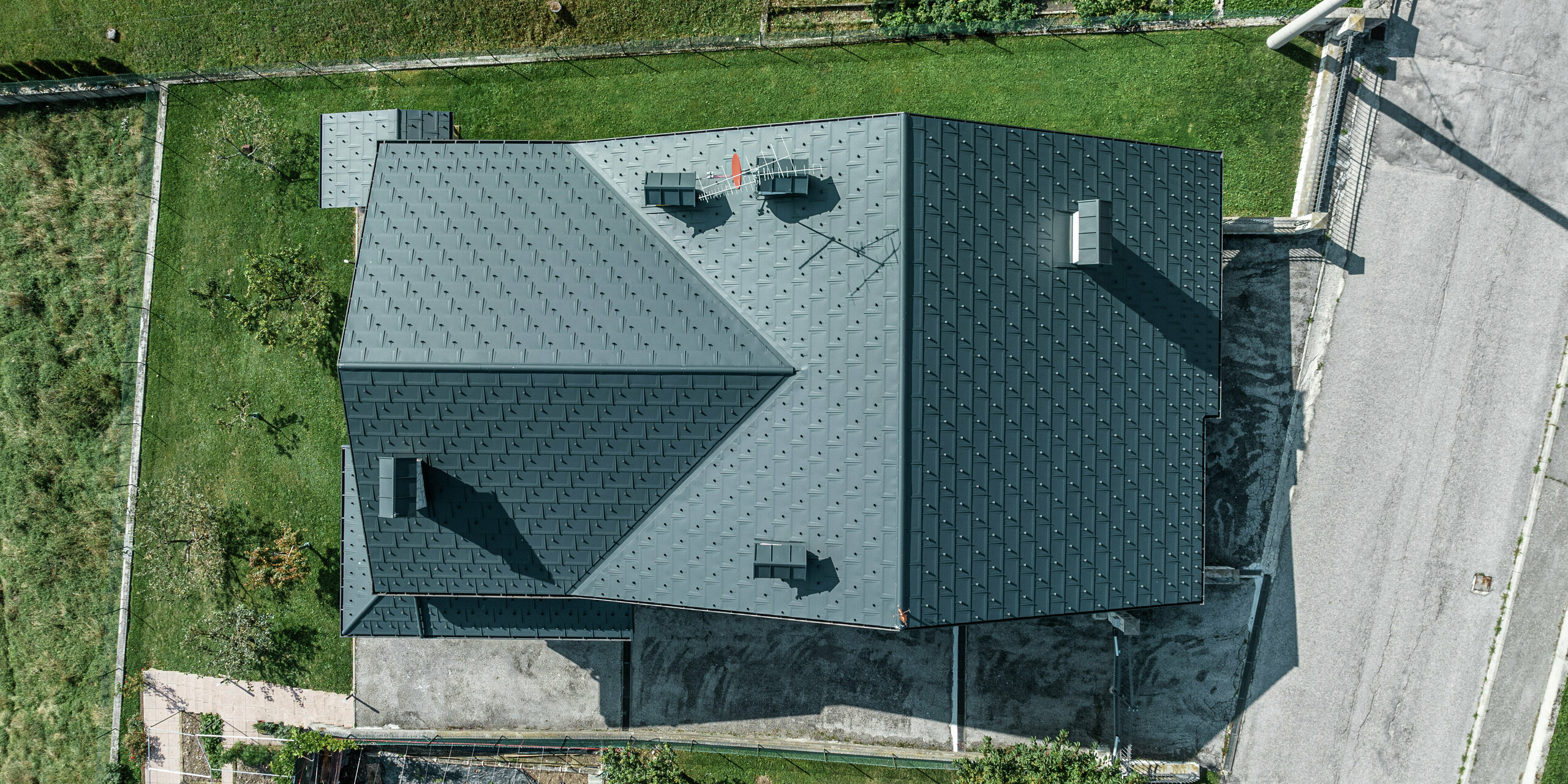 Letecký záber rodinného domu v Gallio s kvalitnou strešnou krytinou PREFA zo strešných panelov R.16 v tmavošedej farbe P.10. Hliníkové strešné riešenie presvedčí moderným vzhľadom, extrémnou odolnosťou voči poveternostným vplyvom a dlhou životnosťou. Snehové zábrany zaisťujú dodatočnú bezpečnosť v alpských regiónoch. Presné spracovanie a premyslený odvodňovací systém zaručujú optimálnu ochranu pred dažďom a snehom. Strecha s nízkymi nárokmi na údržbu pre celé generácie.