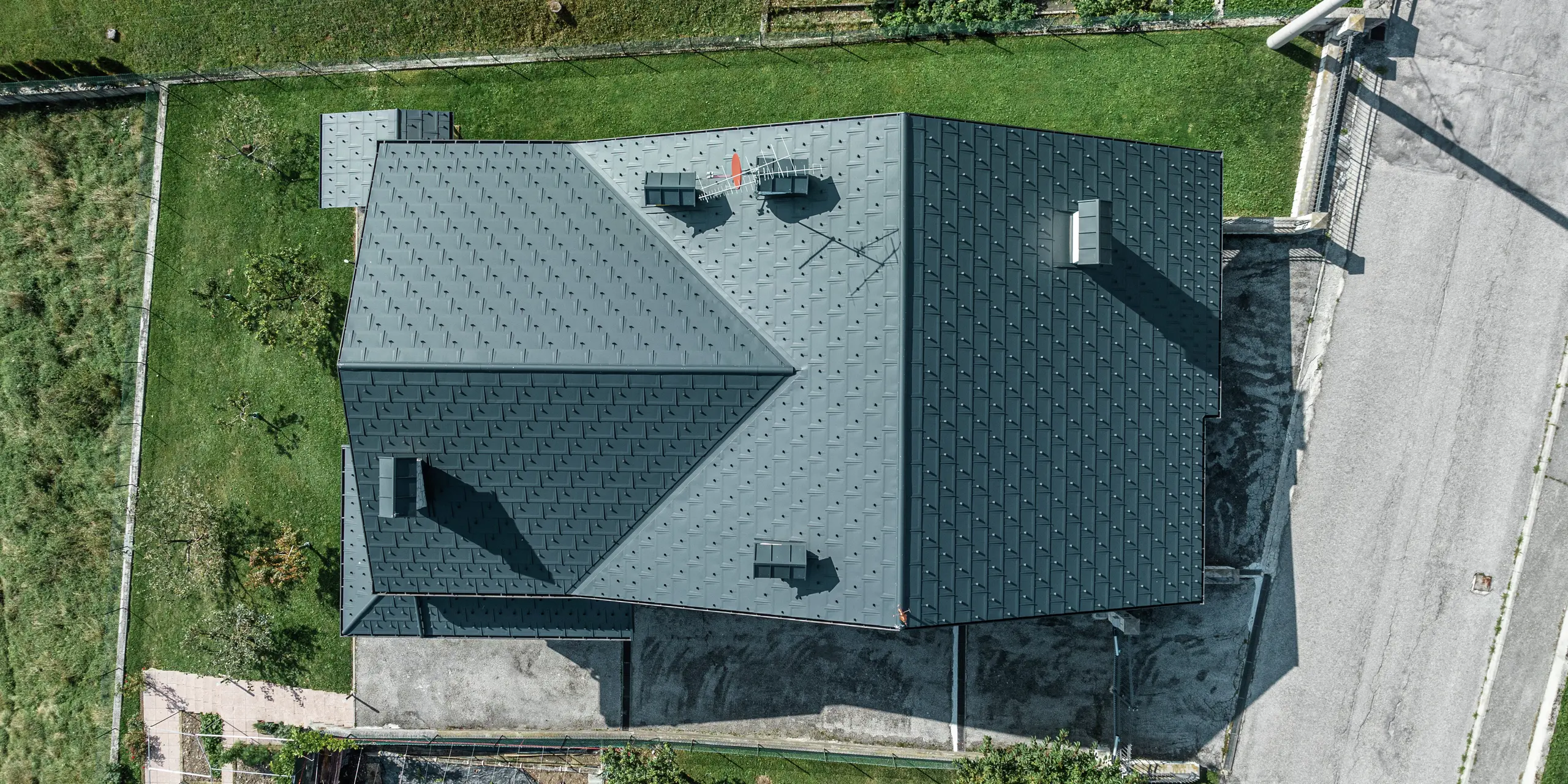 Letecký záber rodinného domu v Gallio s kvalitnou strešnou krytinou PREFA zo strešných panelov R.16 v tmavošedej farbe P.10. Hliníkové strešné riešenie presvedčí moderným vzhľadom, extrémnou odolnosťou voči poveternostným vplyvom a dlhou životnosťou. Snehové zábrany zaisťujú dodatočnú bezpečnosť v alpských regiónoch. Presné spracovanie a premyslený odvodňovací systém zaručujú optimálnu ochranu pred dažďom a snehom. Strecha s nízkymi nárokmi na údržbu pre celé generácie.