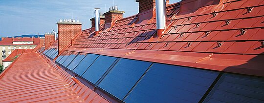 Zaoblená strecha obytného komplexu pokrytá šindľom PREFA a strechou so stojatou drážkou (falcom) – Prefalz – od spoločnosti PREFA v tehlovočervenej farbe.