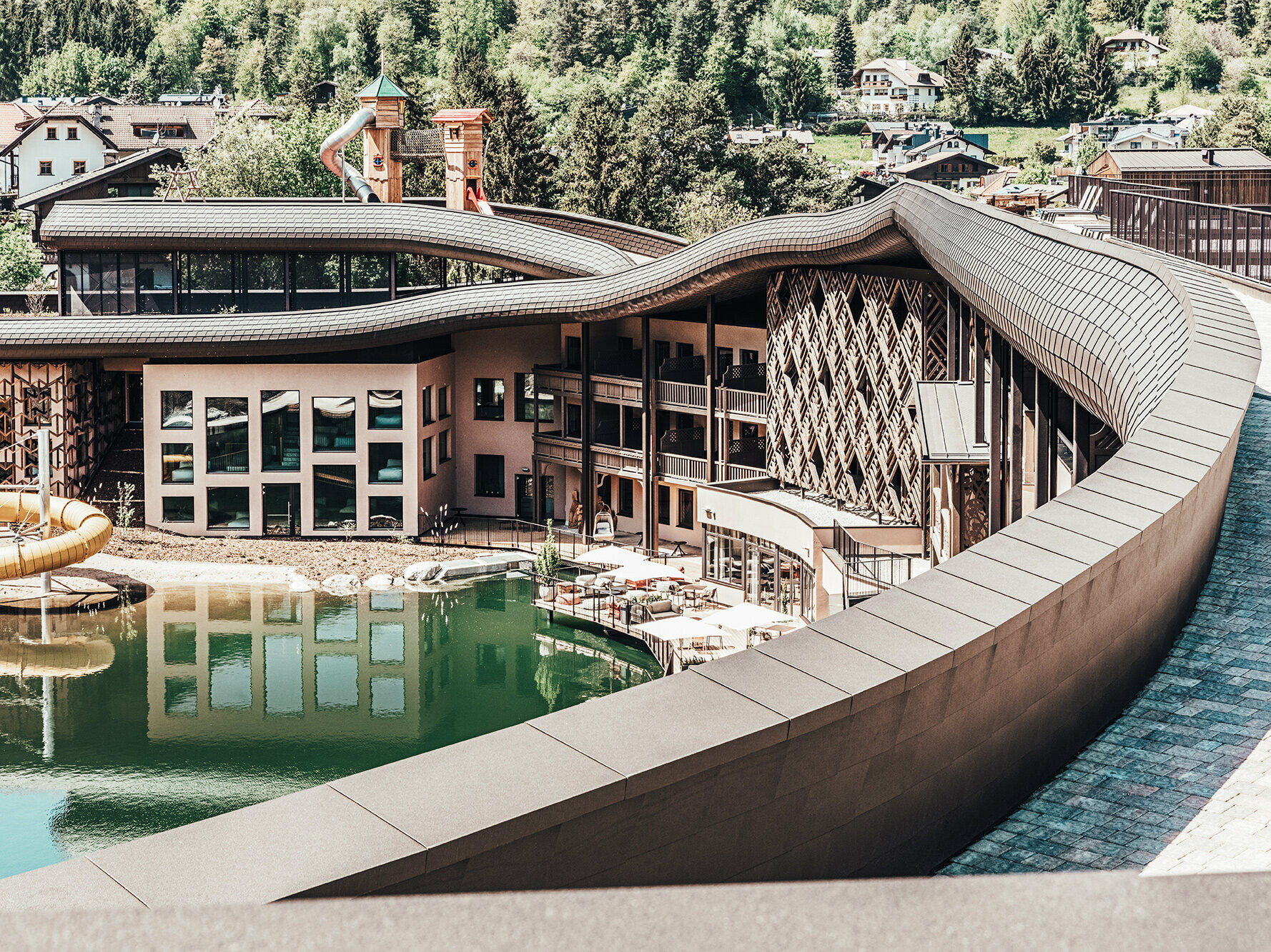 Blick auf das Hotel, die Dachwelle zieht sich über das gesamte Gebäude, ein See ist vor dem Hotel zu sehen