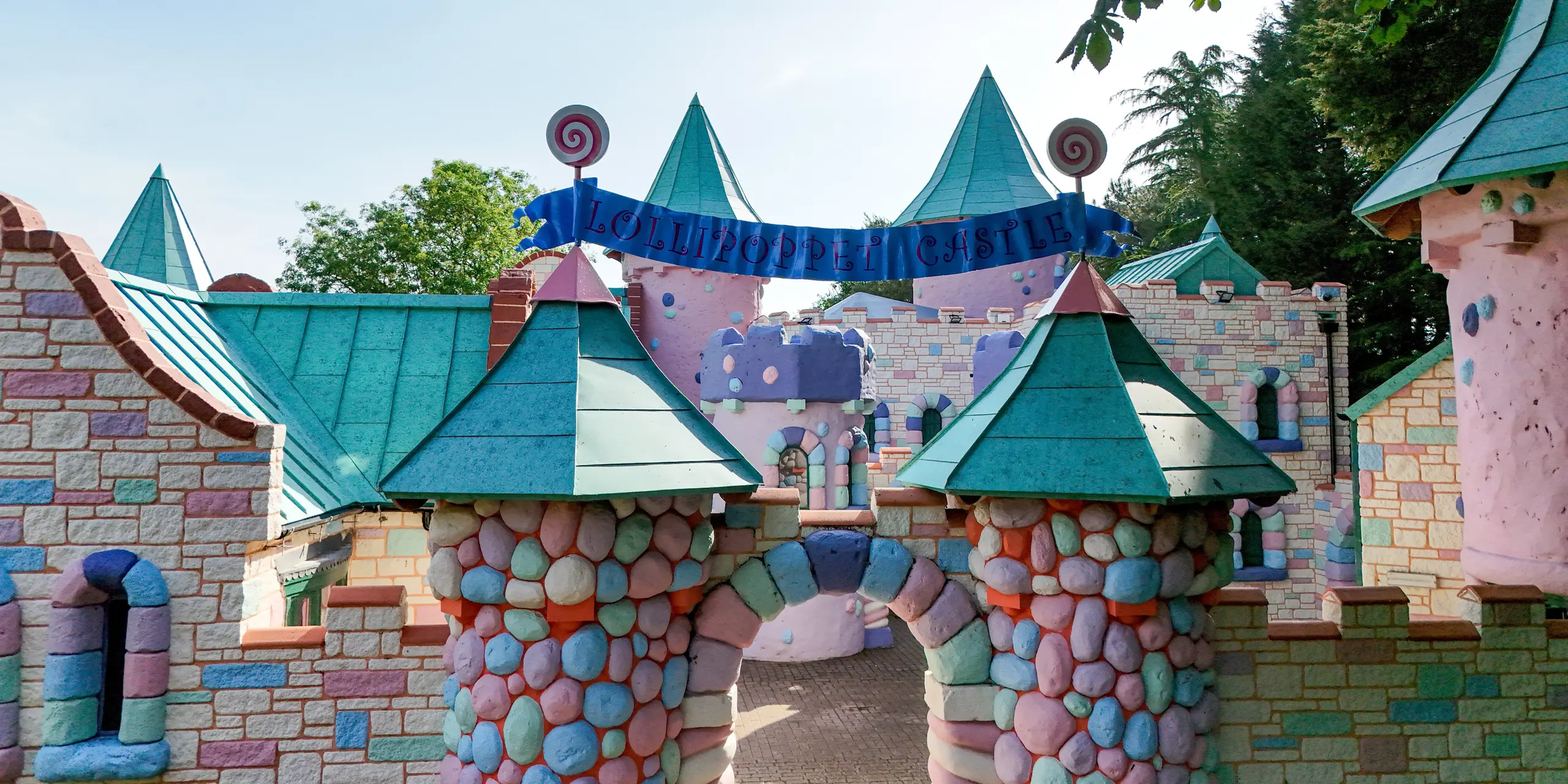 Frontalansicht des Eingangs zur fantasievollen Lollipoppet Castle Anlage im Sundown Adventureland mit farbenfrohen Steinstrukturen, verspielten Rundtürmen und markanten Kegeldächern als starke Eyecatcher. Die PREFALZ Aluminiumdächer in P.10 Patinagrün prägen das Erscheinungsbild und setzen mit ihren präzisen Stehfalzen klare, hochwertige Akzente. Die komplexen Dachformen werden elegant umgesetzt und unterstreichen die gestalterische Freiheit, während das PREFA System durch Langlebigkeit, Korrosionsbeständigkeit und zuverlässigen Schutz bei jeder Witterung überzeugt.
