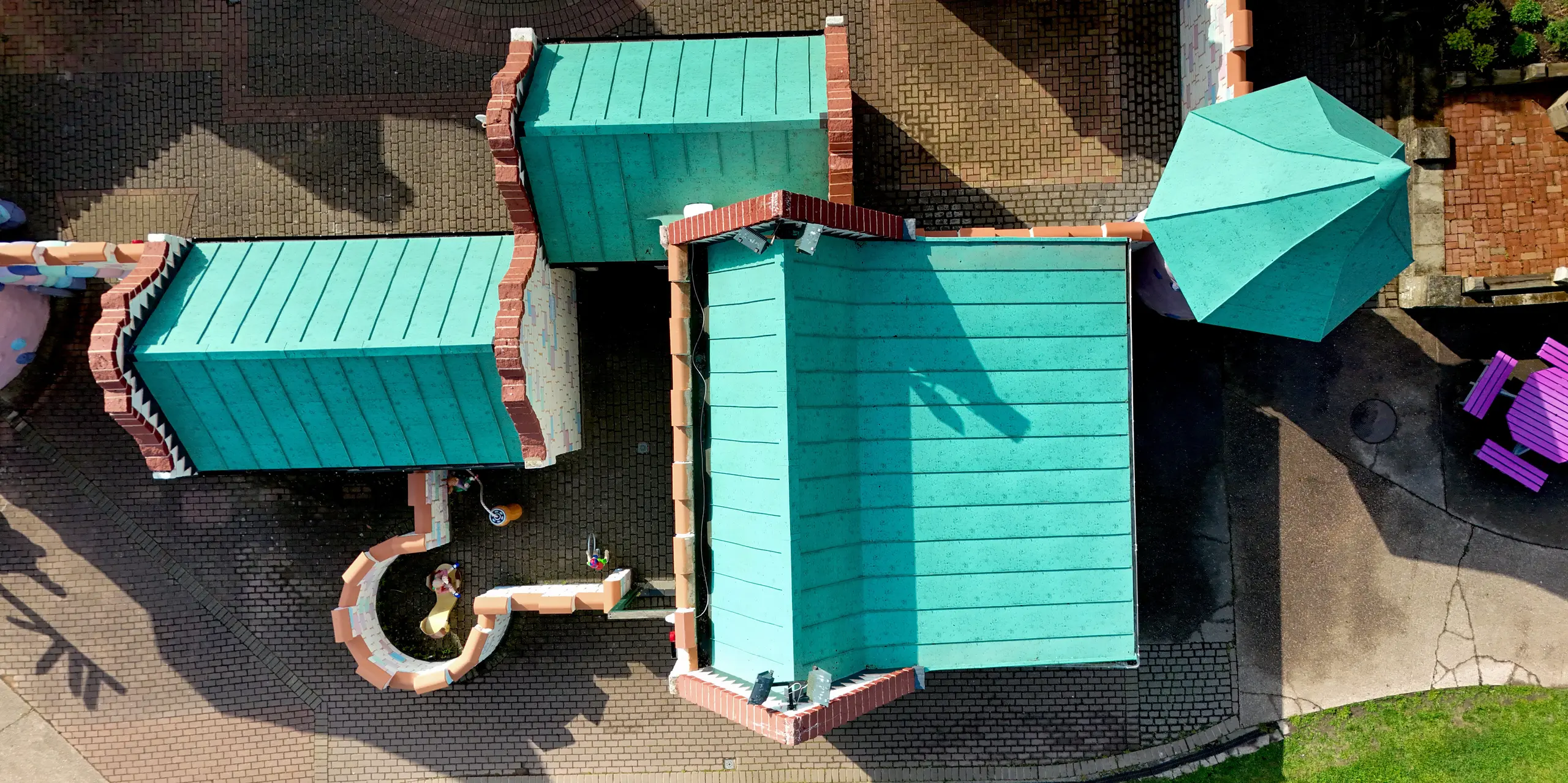 Dynamische Vogelperspektive auf die verspielte Schlossarchitektur im Sundown Adventureland mit mehreren unterschiedlich geneigten Dachflächen, markanten Kanten und klar strukturierten Stehfalzen als visuelle Eyecatcher. Die PREFALZ Aluminiumdächer in P.10 Patinagrün verleihen den Gebäuden eine hochwertige, präzise Anmutung und heben die komplexe Geometrie eindrucksvoll hervor. Dank der hohen Formbarkeit lassen sich selbst anspruchsvolle Details exakt umsetzen, während das PREFA System durch Langlebigkeit, Korrosionsbeständigkeit und zuverlässigen Schutz gegenüber Witterungseinflüssen überzeugt.