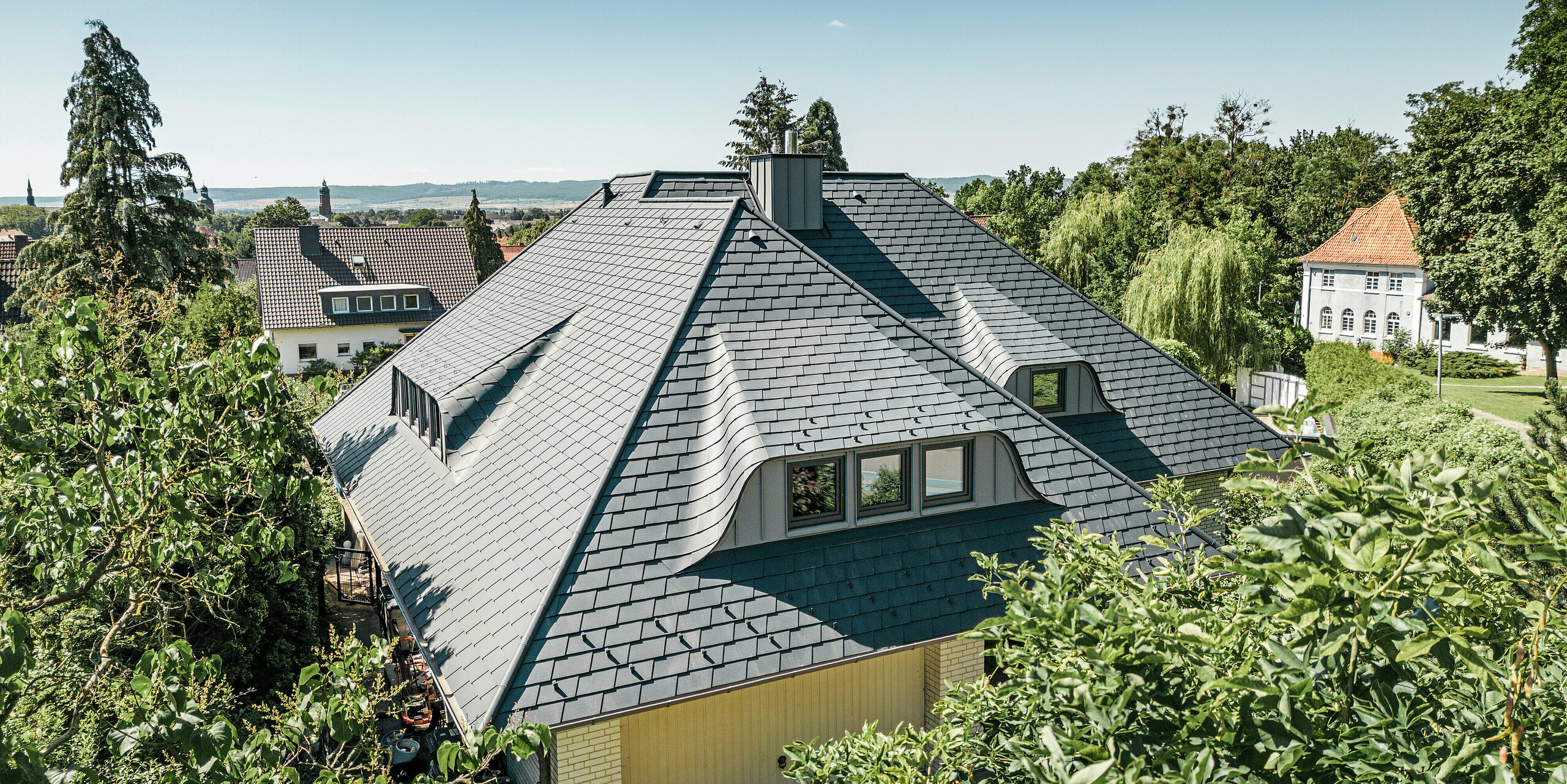 Strecha so zakrivenými vikiermi na rodinnom dome v Einbecku pokrytá strešnými šindľami PREFA v antracitovej farbe P.10