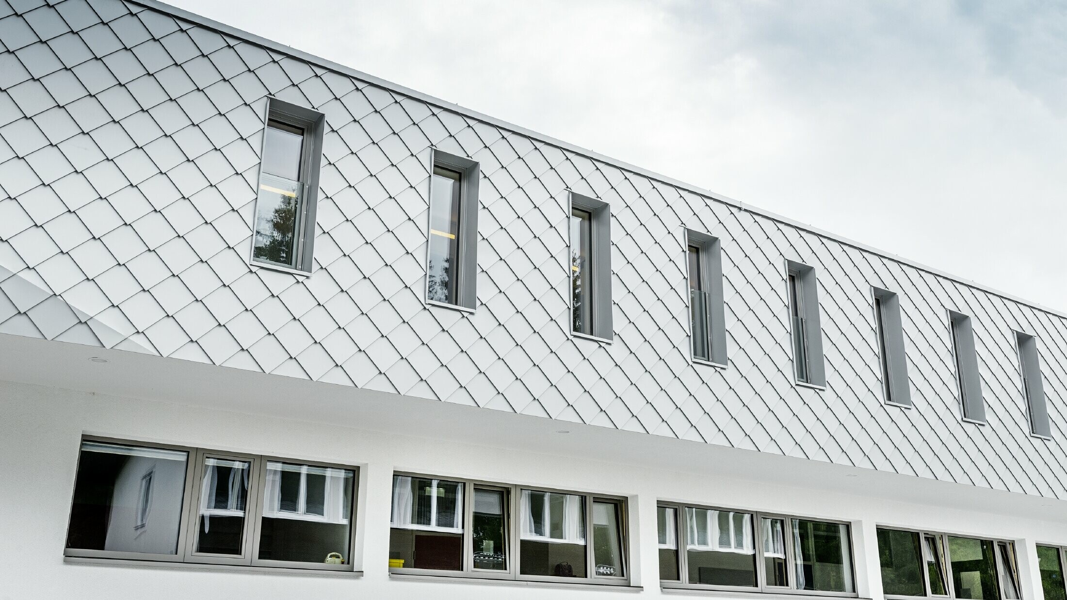 Novo vybudovaná materská škola v Kaprune s modernou hliníkovou fasádou s PREFA fasádnou šablónou vo farbe prefa biela