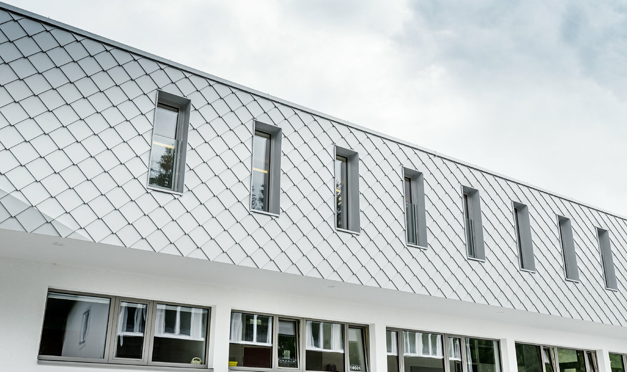 Novo vybudovaná materská škola v Kaprune s modernou hliníkovou fasádou s PREFA fasádnou šablónou vo farbe prefa biela