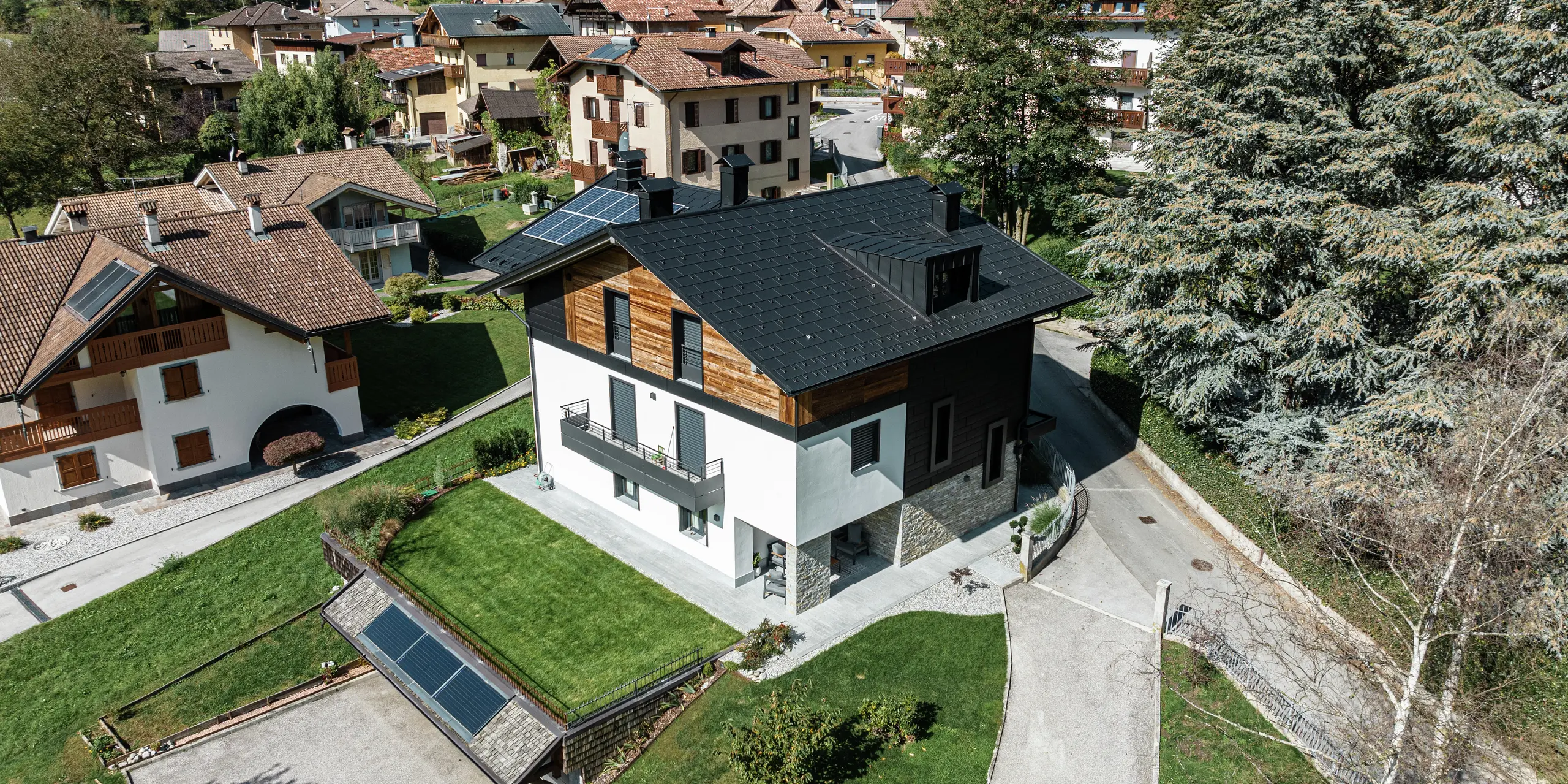 Pohľad z vtáčej perspektívy na moderný zrekonštruovaný obytný dom v Pelugu v Taliansku so strešnými panelmi PREFA R.16 vo farbe P.10 antracit a fasádnymi panelmi PREFA Siding.X. Kombinácia hliníka, dreva a kameňa zabezpečuje harmonickú, poveternostným vplyvom odolnú a udržateľnú architektúru