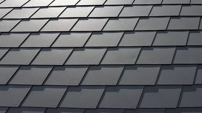 Detail strešnej krytiny so šindľom PREFA vo farbe P.10 tmavošedá. Šindle sú rovnomerne usporiadané a je na nich vidieť výrazný hliníkový povrch odolný voči poveternostným vplyvom, ktorý ponúka matný a štruktúrovaný vzhľad.