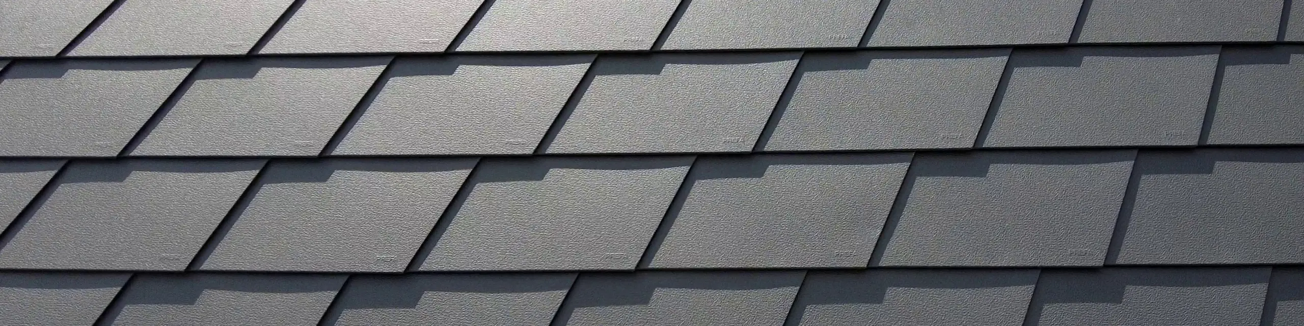 Detail strešnej krytiny so šindľom PREFA vo farbe P.10 tmavošedá. Šindle sú rovnomerne usporiadané a je na nich vidieť výrazný hliníkový povrch odolný voči poveternostným vplyvom, ktorý ponúka matný a štruktúrovaný vzhľad.