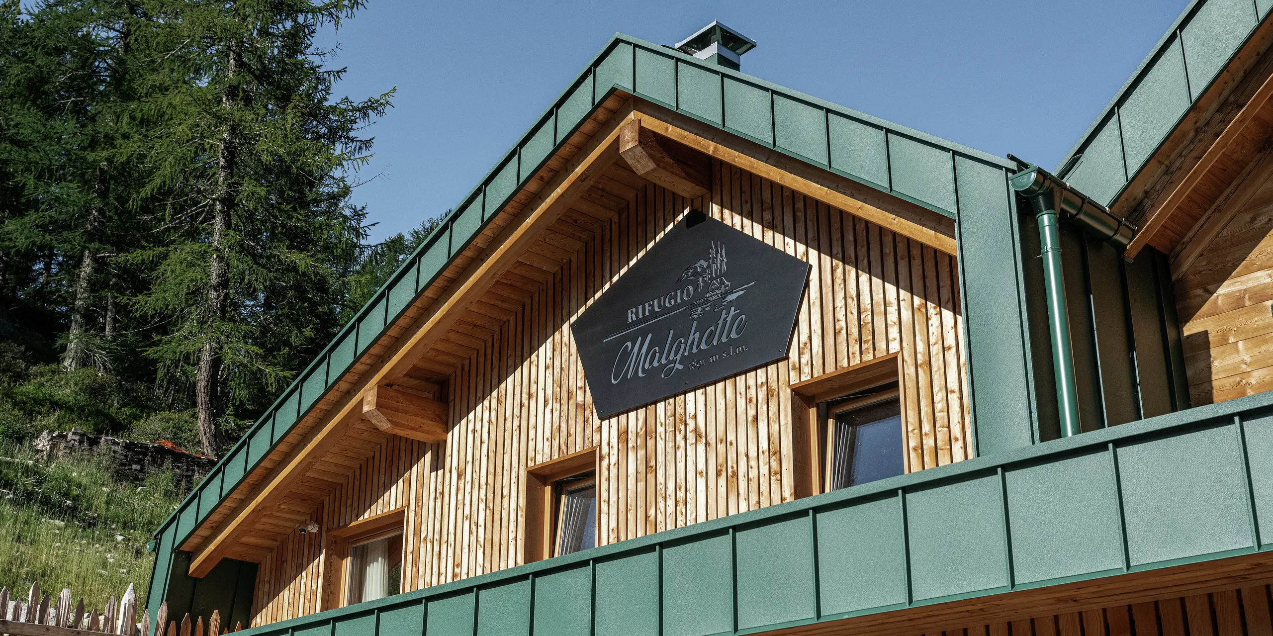 Detailný pohľad na fasádu Rifugio Malghette s PREFALZ vo farbe P.10 machovozelená - odolná, bezúdržbová a dokonale kombinovaná s prírodným drevom. Odolný hliníkový obklad spoľahlivo chráni chatu pred extrémnymi poveternostnými podmienkami vo vysokohorských polohách