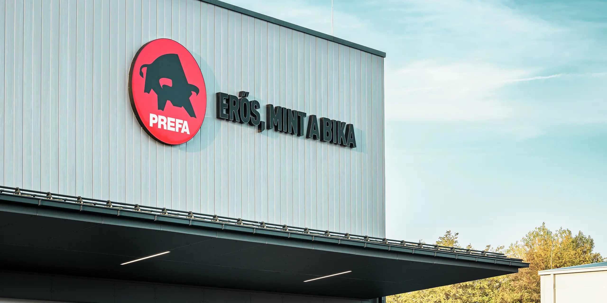 Výrazné logo PREFA a maďarský slogan „Erős, mint a bika“ („Silná ako býk“) charakterizujú fasádu areálu PREFA v Törökbálinte. Opláštenie hliníkovými lamelami PREFA Siding v striebornej metalíze zabezpečuje moderný vzhľad, maximálnu odolnosť voči poveternostným vplyvom a trvanlivosť. Precízne spracovanie zdôrazňuje vysoké štandardy kvality spoločnosti PREFA a odráža silu značky.