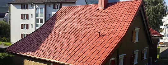 Sedlová strecha pokrytá hliníkovým strešným panelom PREFA. Strecha v tehlovočervenej farbe so snehovými zábranami a komínom