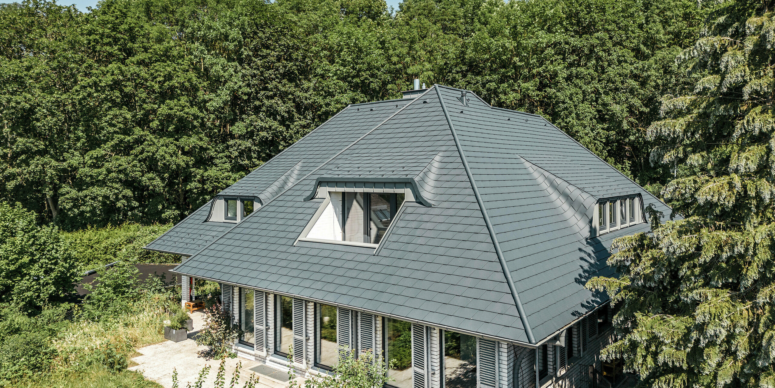 Samostatne stojaci dom s veľkolepou strechou pokrytou strešnými šindľami PREFA v antracitovej farbe P.10