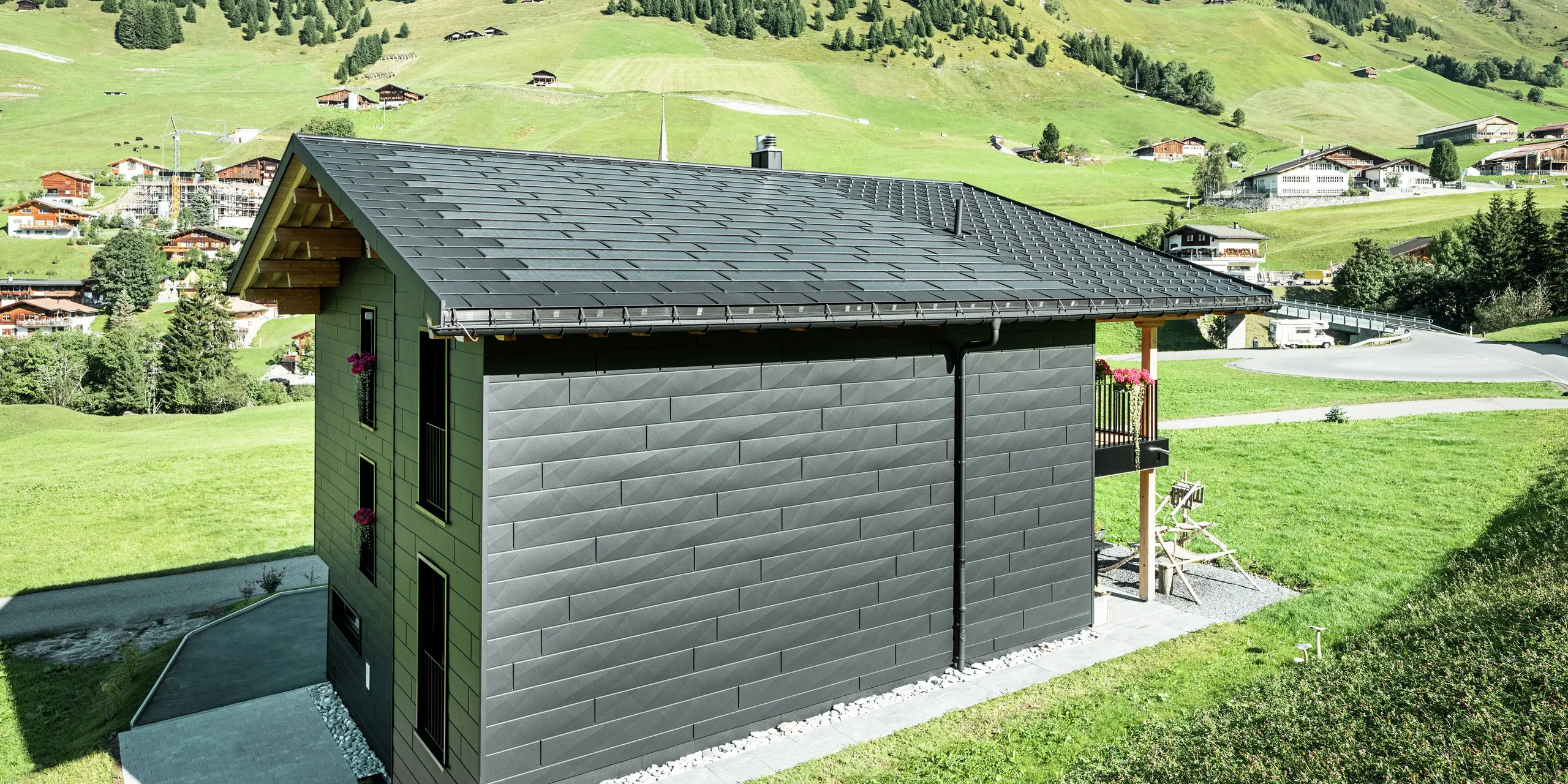 Bočný pohľad na rodinný dom s jasným výhľadom na strešné a fasádne produkty PREFA z hliníka. Integrované strešné panely a strešné panely R.16 v čiernej farbe P.10 nielenže poskytujú ochranu pred poveternostnými vplyvmi, ale aj moderný, nezameniteľný vzhľad. PREFA odvodňovací žľab a zvod sú perfektne integrované a fasádne panely Siding.X dodávajú budove nezameniteľný charakter.