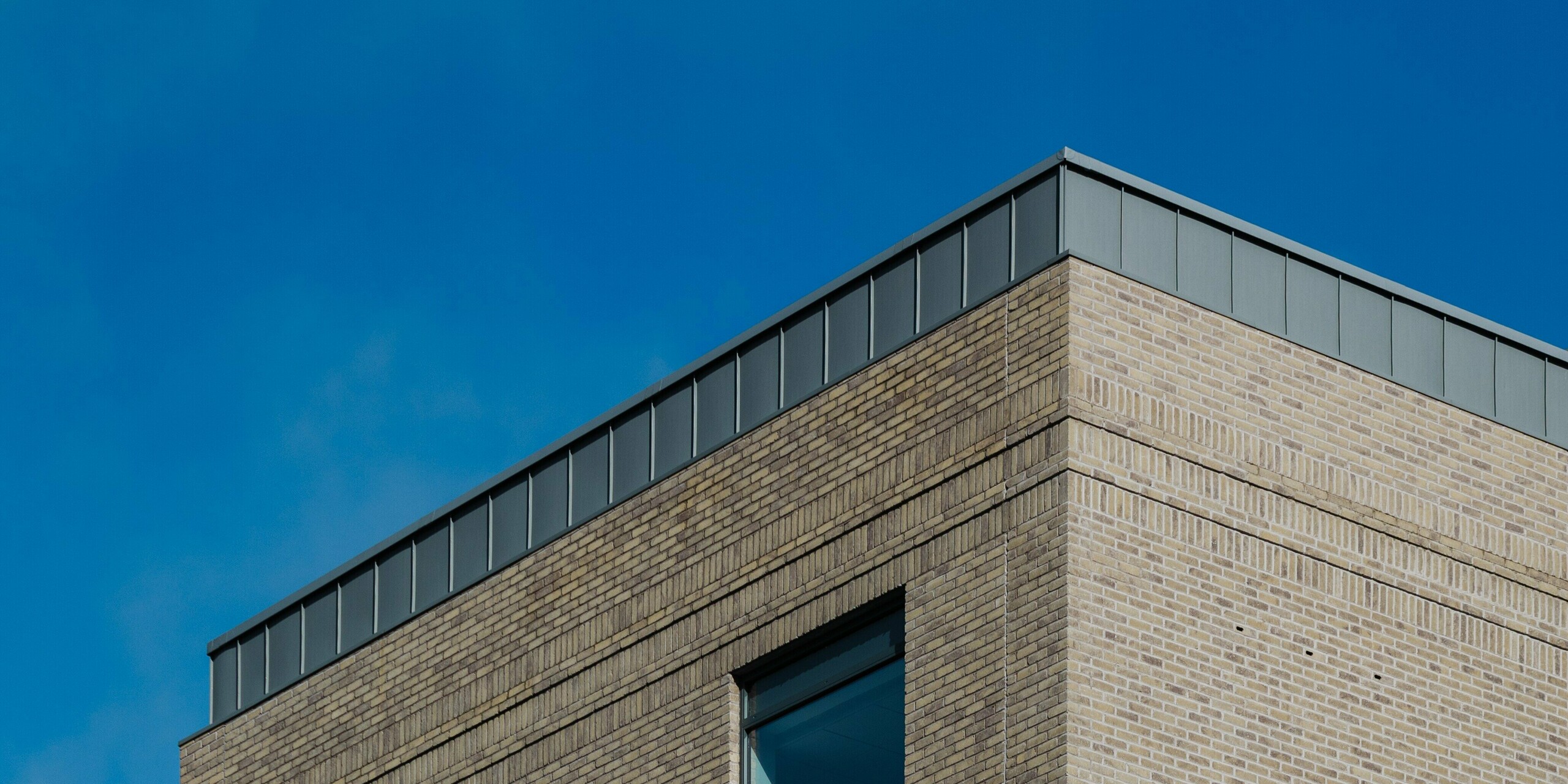 Das Northern Regional College in Ballymena zeigt sich als markanter Bildungsbau mit klaren Linien und hochwertiger Materialität. Die Fassade aus hellem Klinker wird von vertikal verlegten PREFALZ Aluminium-Stehfalzbahnen in Patinagrau gekrönt, die als visueller Eyecatcher dienen. Das langlebige PREFA Aluminium überzeugt durch Witterungsbeständigkeit, geringes Gewicht und elegante Optik. Der ruhige Grauton setzt einen spannenden Kontrast zu Glasflächen und Himmel und verleiht dem Gebäude zeitlose architektonische Präsenz.
