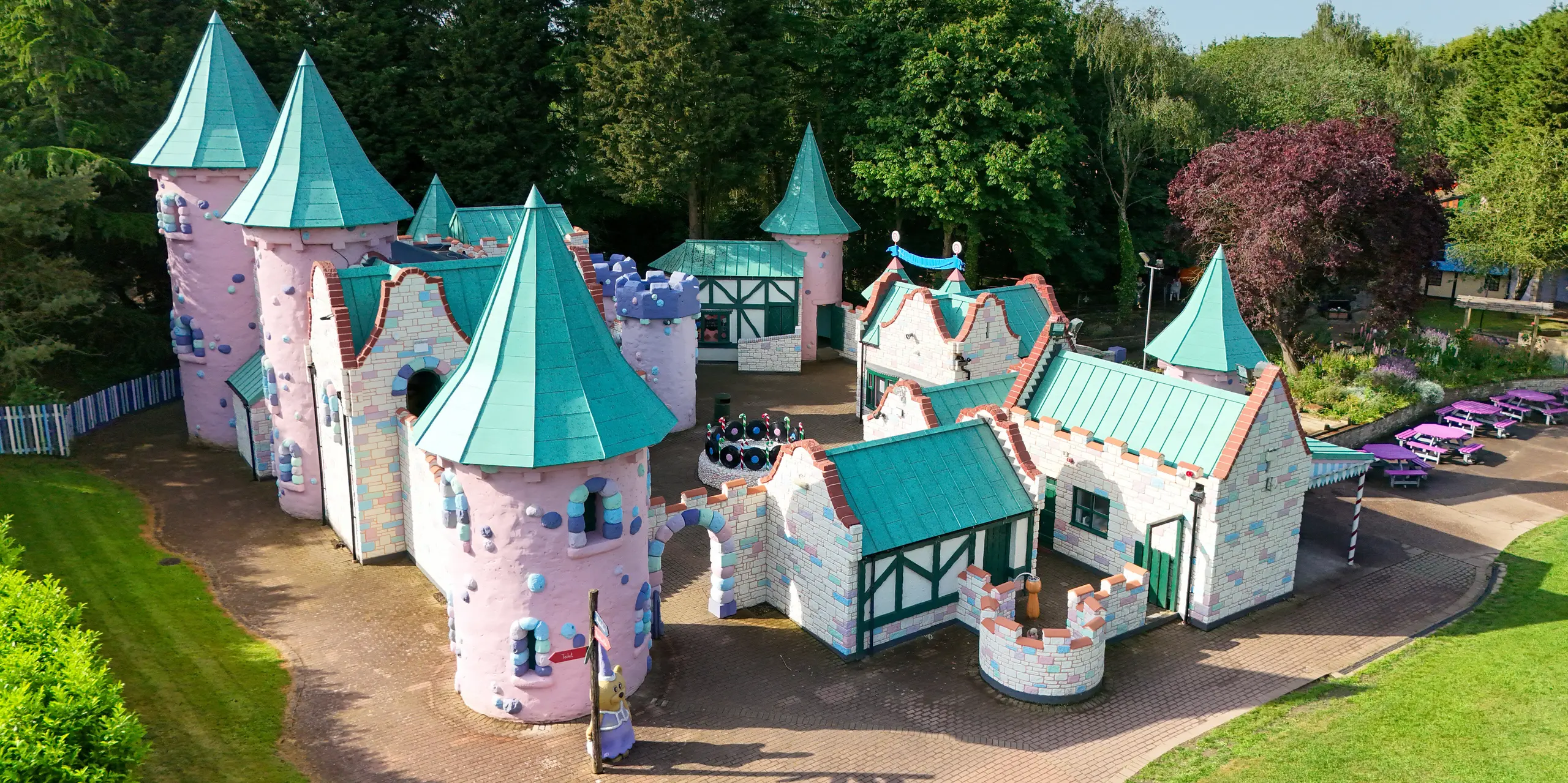 Frontale Ansicht der märchenhaften Schlosskulisse im Sundown Adventureland mit zahlreichen verspielten Türmen, spitzen Kegeldächern und detailreichen Fassaden in Pastellfarben. Die markanten PREFALZ Aluminiumdächer in P.10 Patinagrün fungieren als zentrale Eyecatcher und betonen die fantasievollen Formen mit präzisen Stehfalzen. Unterschiedliche Dachneigungen und komplexe Geometrien werden elegant umgesetzt. Gleichzeitig überzeugen die PREFA Dächer durch hohe Langlebigkeit, Korrosionsbeständigkeit und zuverlässigen Schutz – ideal für dauerhaft beeindruckende Freizeitarchitektur.