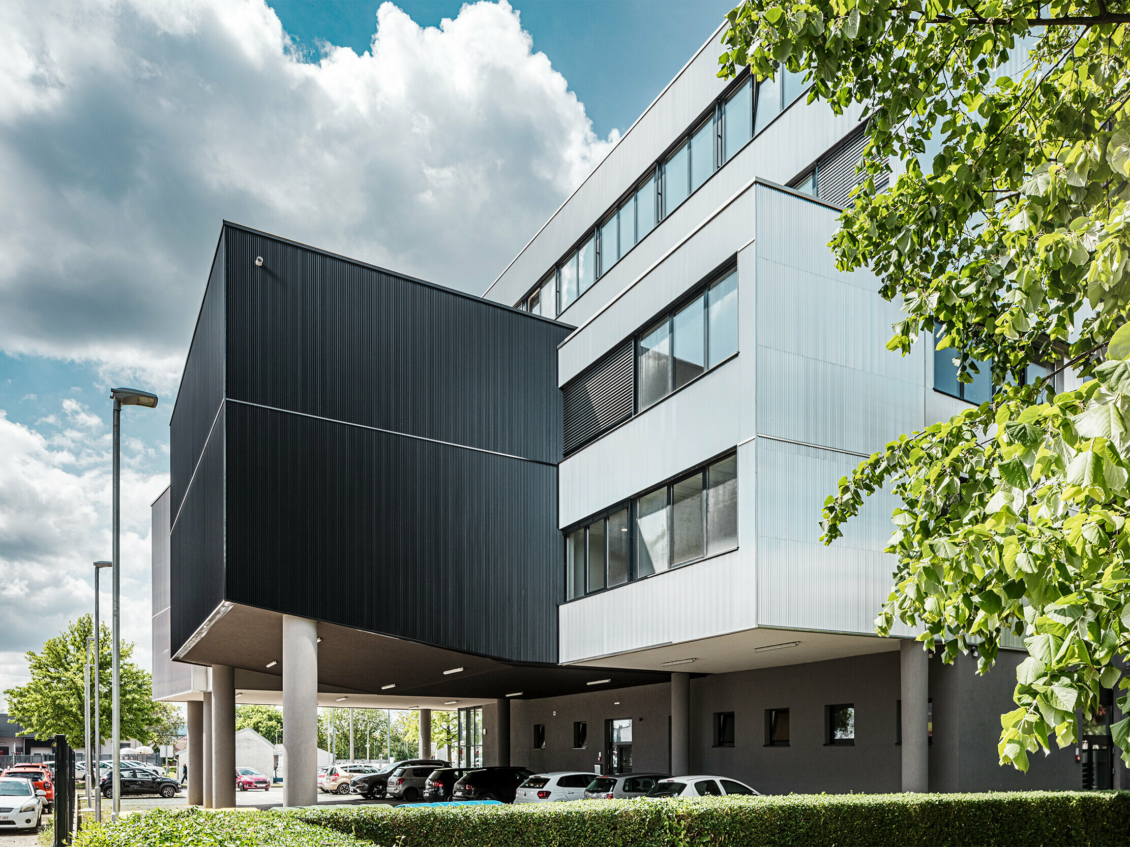 Moderná administratívna budova hudobnej školy v Bjelovare v Chorvátsku má výraznú hliníkovú fasádu z lisovaných prelamovaných profilov PREFA. Čierne a strieborné eloxované fasádne plochy vytvárajú jasné architektonické kontrasty a dodávajú budove charakter a hĺbku. Vertikálne uložené profily vytvárajú elegantnú štruktúru so zaujímavým efektom svetla a tieňa. Vďaka robustnému, korózii odolnému hliníkovému povrchu sú fasádne prvky mimoriadne odolné a ľahko sa udržiavajú. Skryté upevnenie zaisťuje rovnomerný, kvalitný vzhľad. Táto zavesená, odvetraná fasáda PREFA spája dizajn, techniku a funkčnosť.