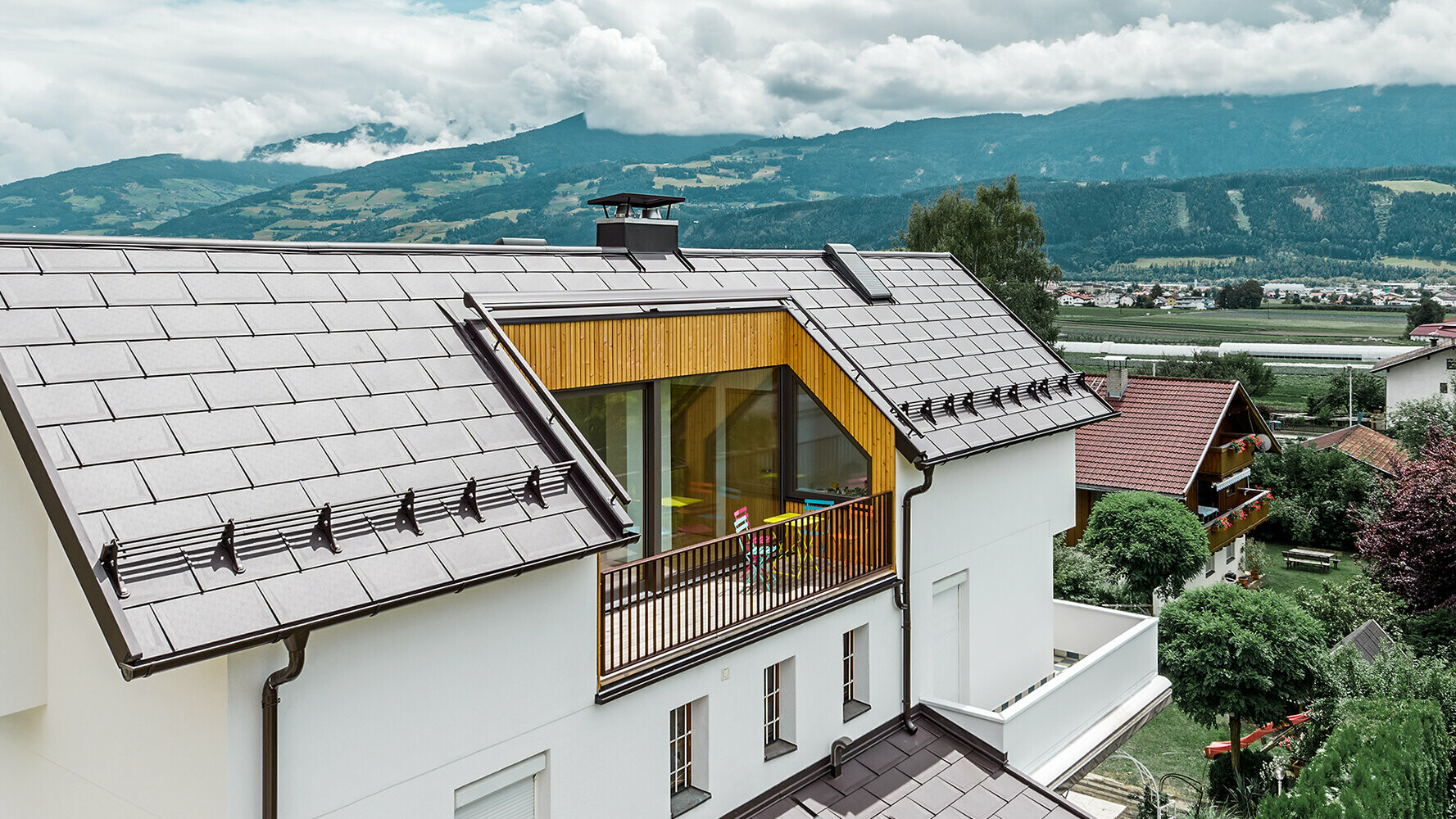 Obytný dom zastrešený hliníkovým strešným panelom PREFA R.16 v orieškovej hnedej farbe s veľkým balkónom a svetlou omietnutou fasádou.