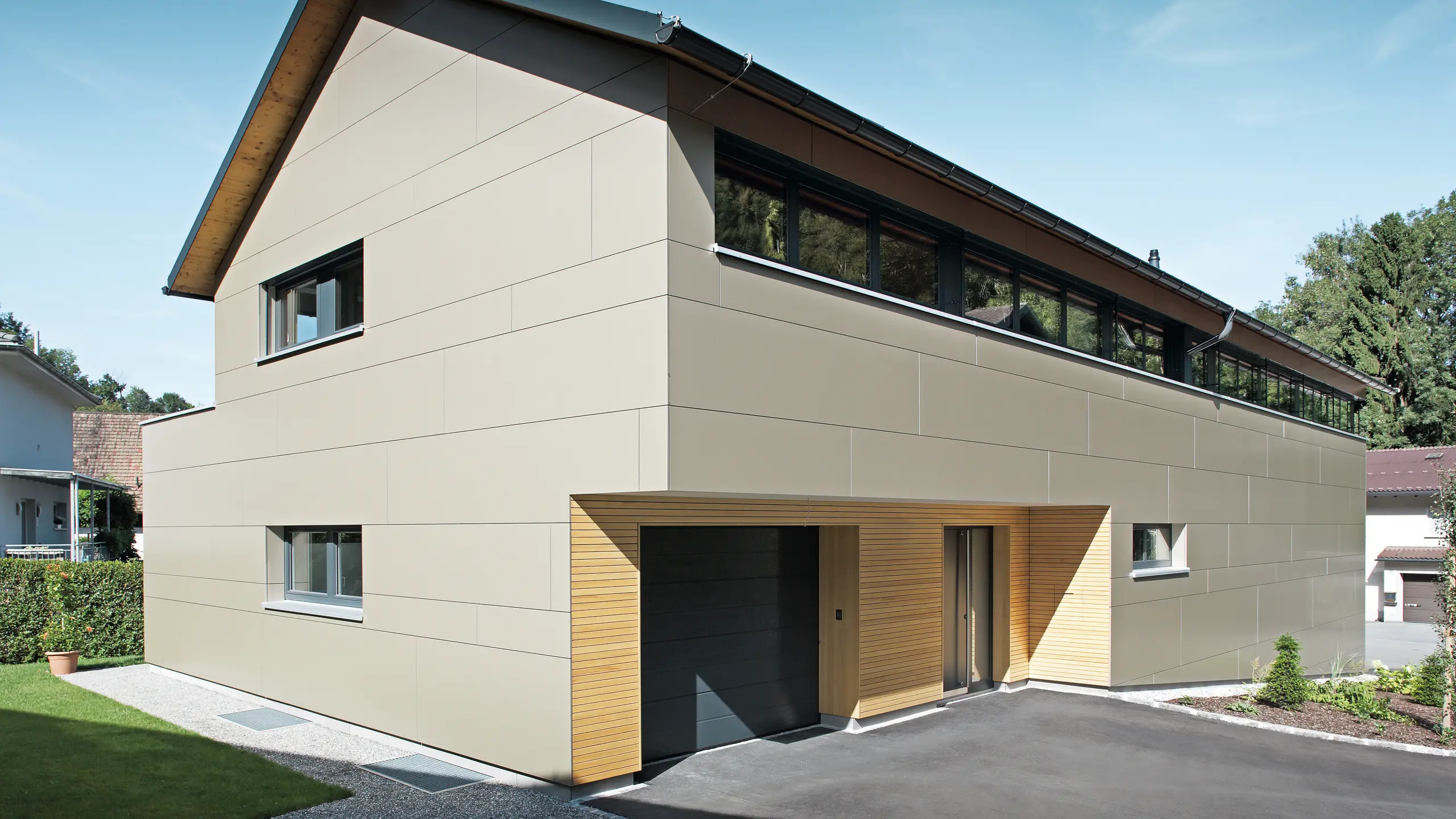Elegantný rodinný dom v Hohenemse, vybavený kompletným systémom PREFA. Fasádu tvoria hliníkové kompozitné panely v bronzovej metalíze, ktoré vytvárajú moderný a čistý vzhľad, zatiaľ čo drevené prvky pri vstupe do garáže vyžarujú teplo a prirodzenosť. Strecha je pokrytá falcovanými škridlami PREFA vo farbe P.10 antracitová, ktoré spolu s fasádou vytvárajú celkový architektonický koncept a účinne chránia dom.