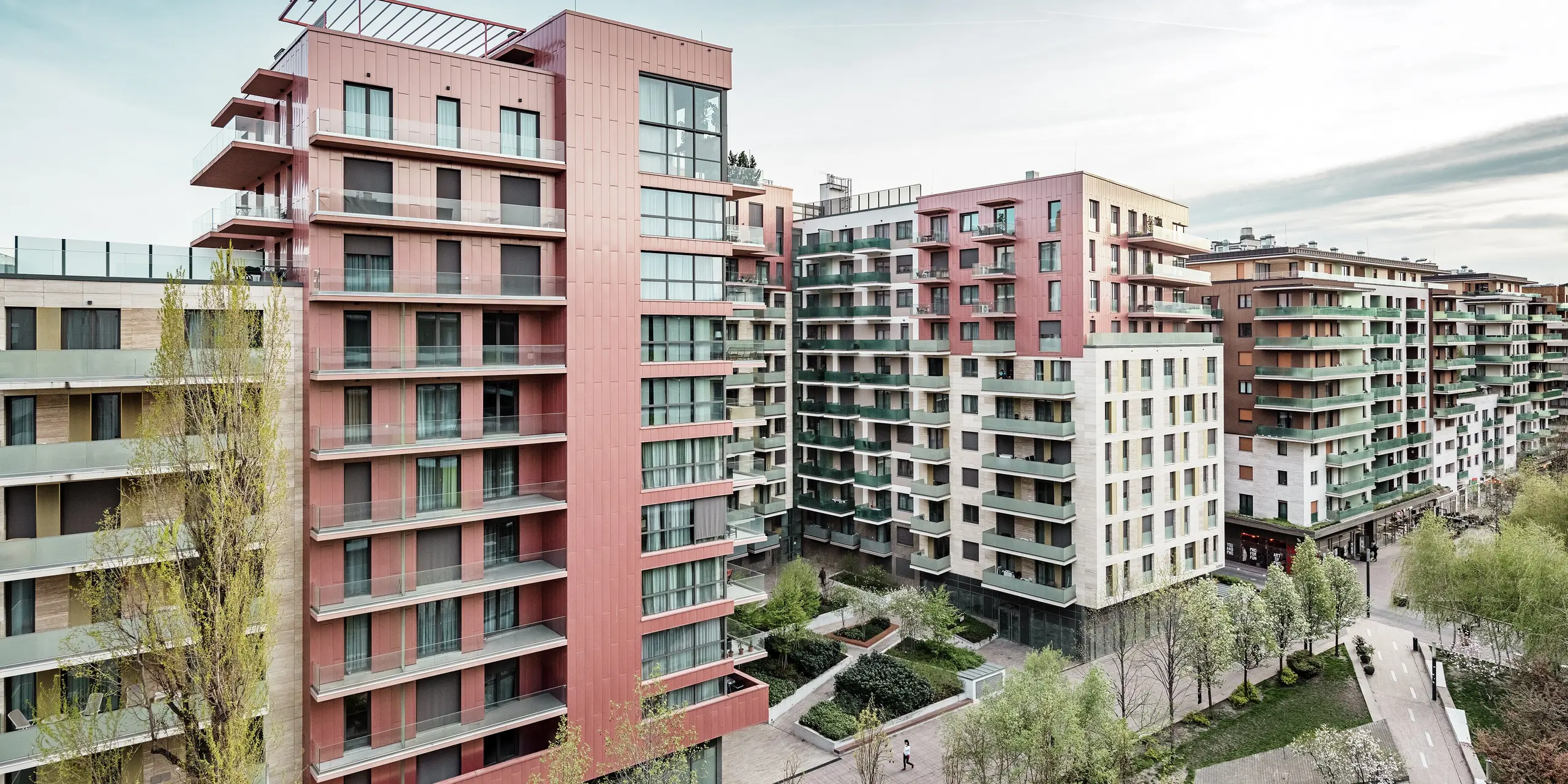 Panoramatický pohľad na obytný komplex Grand Corvin v novo zrekonštruovanej štvrti Corvin v Budapešti. Výrazné časti budovy sú pokryté viac ako 800 m² fasádnych panelov PREFA Siding s vertikálnou pokládkou a špeciálnou farbou lososová metalíza. Odolný hliníkový obklad vytvára architektonické akcenty, harmonicky zapadá do mestskej štruktúry a podčiarkuje vysokú kvalitu a moderný charakter nového obytného komplexu pozdĺž promenády Corvin.