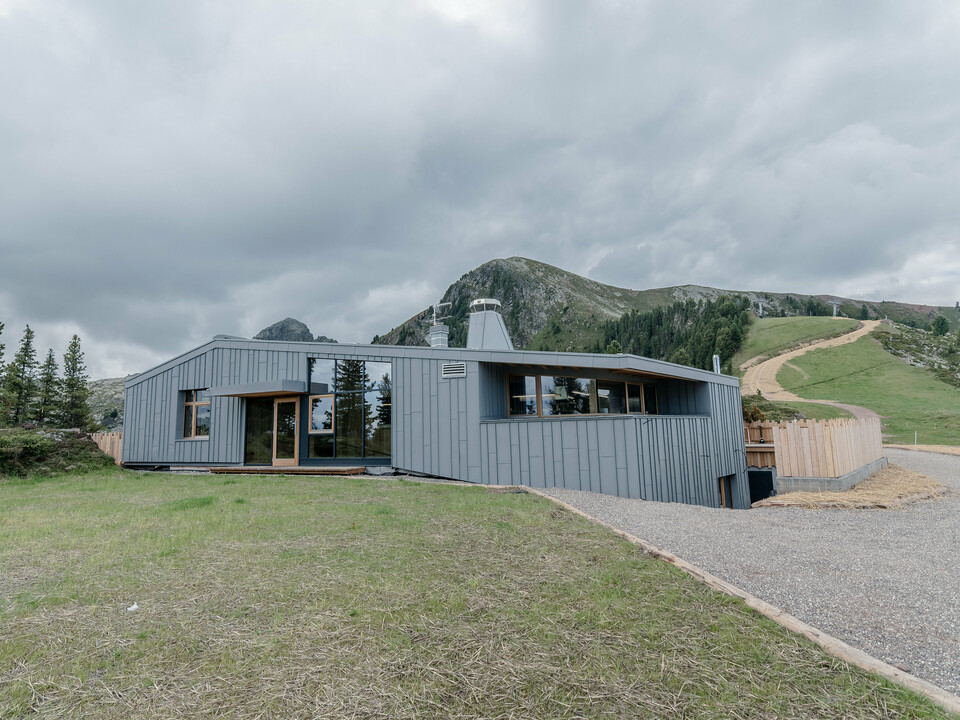 Ristorante Busabelle, vsadená do idylickej horskej krajiny, je pokrytá šikmým zrkadlovým obkladom so stojatou drážkou zo svetlošedej farby PREFALZ, ktorý zvýrazňuje modernú architektúru a vytvára harmonické spojenie s okolitou prírodou. Vstupný priestor má veľké presklené plochy. V pozadí môžete vidieť stožiare pre systém sedačkovej lanovky.