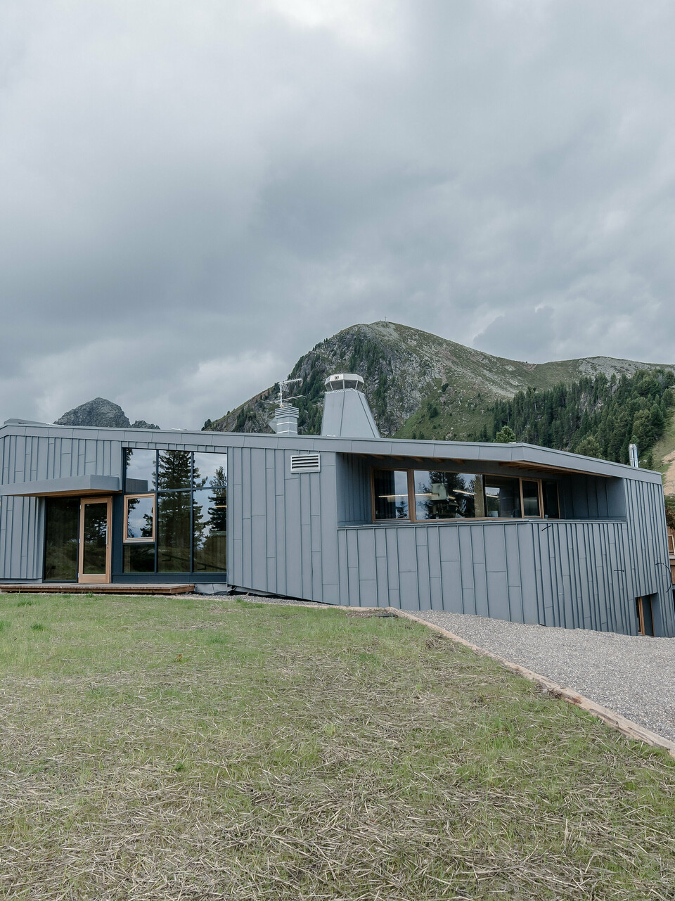 Ristorante Busabelle, vsadená do idylickej horskej krajiny, je pokrytá šikmým zrkadlovým obkladom so stojatou drážkou zo svetlošedej farby PREFALZ, ktorý zvýrazňuje modernú architektúru a vytvára harmonické spojenie s okolitou prírodou. Vstupný priestor má veľké presklené plochy. V pozadí môžete vidieť stožiare pre systém sedačkovej lanovky.