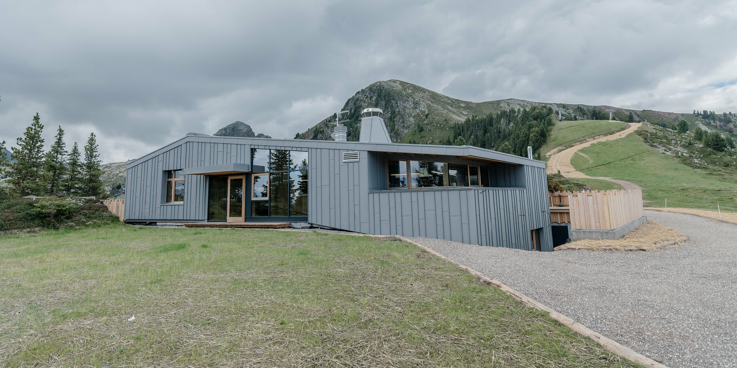 Ristorante Busabelle, vsadená do idylickej horskej krajiny, je pokrytá šikmým zrkadlovým obkladom so stojatou drážkou zo svetlošedej farby PREFALZ, ktorý zvýrazňuje modernú architektúru a vytvára harmonické spojenie s okolitou prírodou. Vstupný priestor má veľké presklené plochy. V pozadí môžete vidieť stožiare pre systém sedačkovej lanovky.