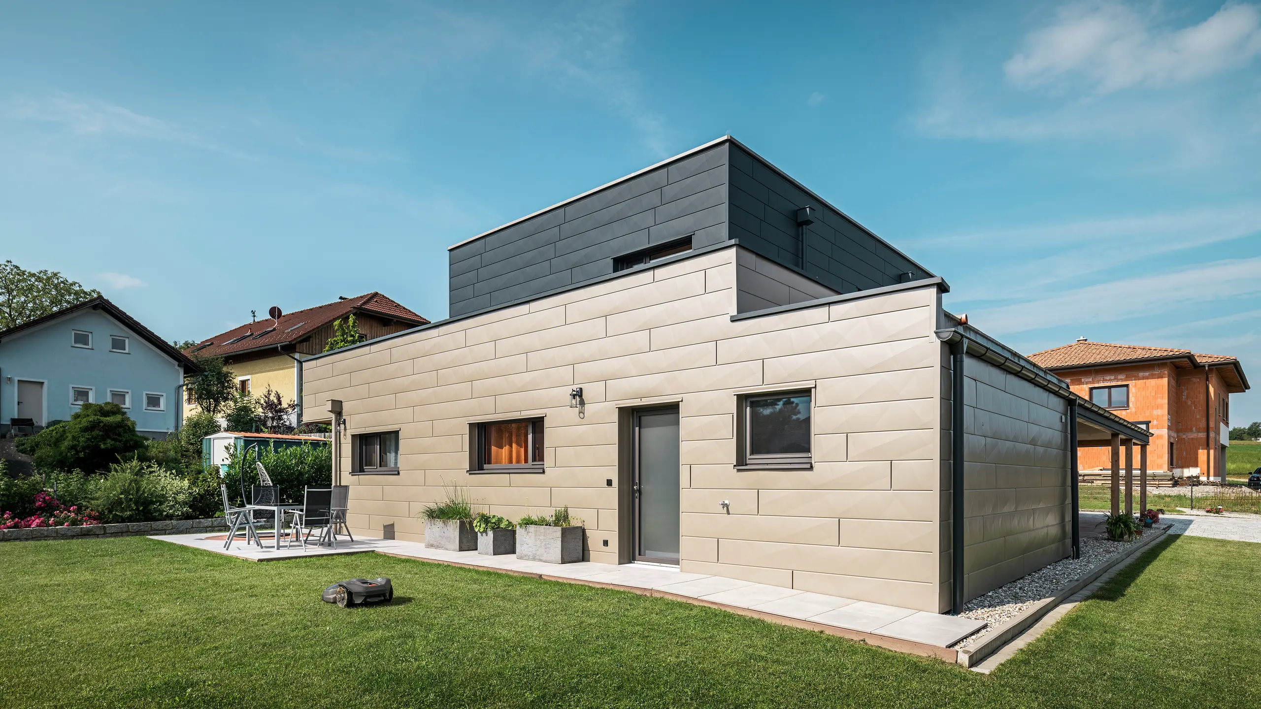 Moderný rodinný dom vo Wippenhame v Rakúsku s dvojfarebnou hliníkovou fasádou PREFA v bronzovej a antracitovej farbe. Fasáda je navrhnutá s fasádnymi panelmi Siding.X, ktoré poskytujú elegantný a moderný vzhľad. Integrované odvodnenie strechy PREFA so zberným kotlíkom na vodu a odvodňovacím zvodom, ako aj upravená záhrada s terasou podčiarkujú moderný dizajn domu.